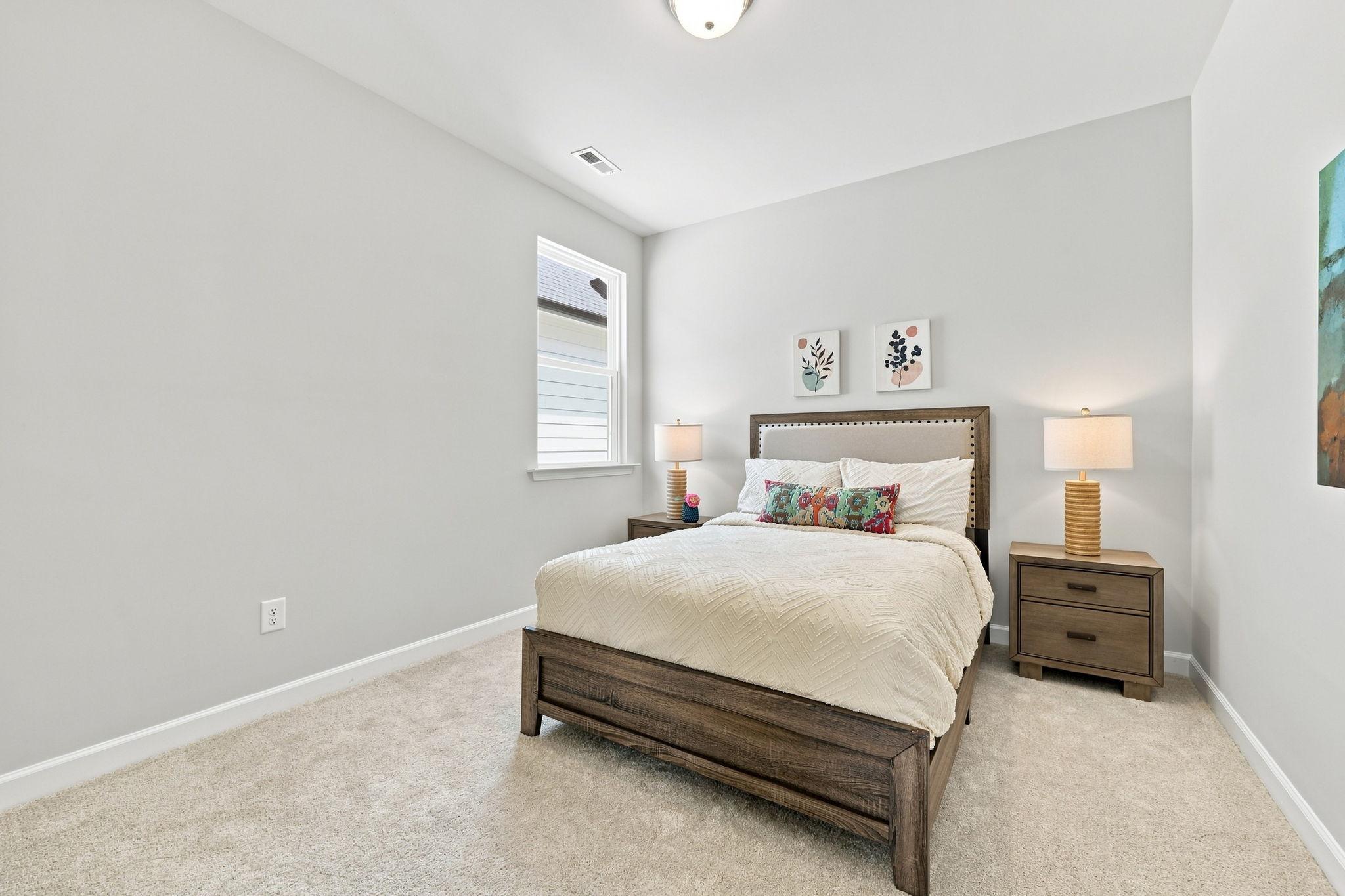 Spacious secondary bedroom in The Jordan A featuring a queen-sized bed, wooden nightstands, and neutral decor.