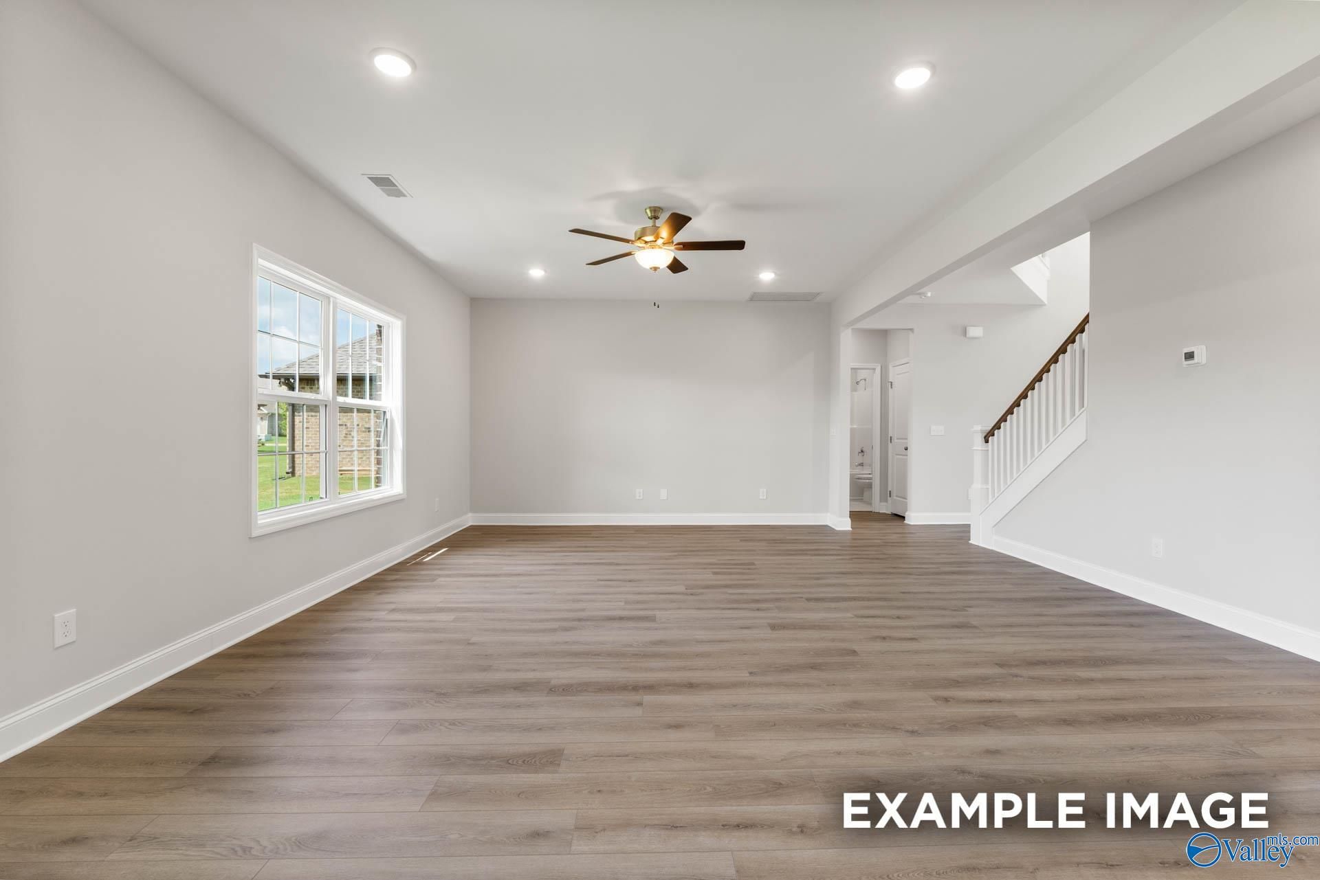 Spacious living room with hardwood floors, ceiling fan, and large windows in The Madison A 5-bedroom home by Davidson Homes in Pikes Ridge, Meridianville, Alabama