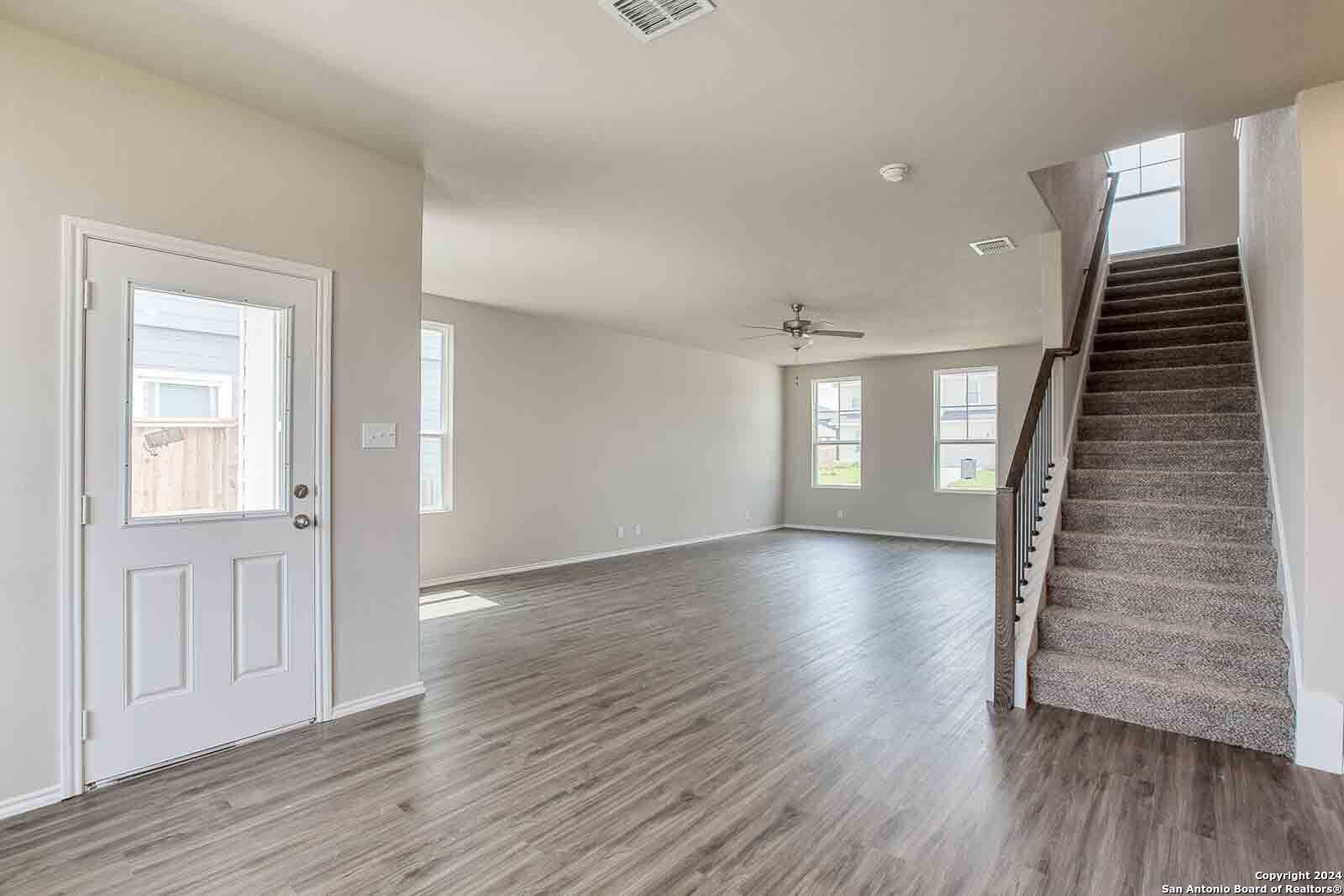 Bright open entryway with gray hardwood floors, white front door, carpeted staircase, and large windows in Davidson Homes The Murray H, Seguin Texas