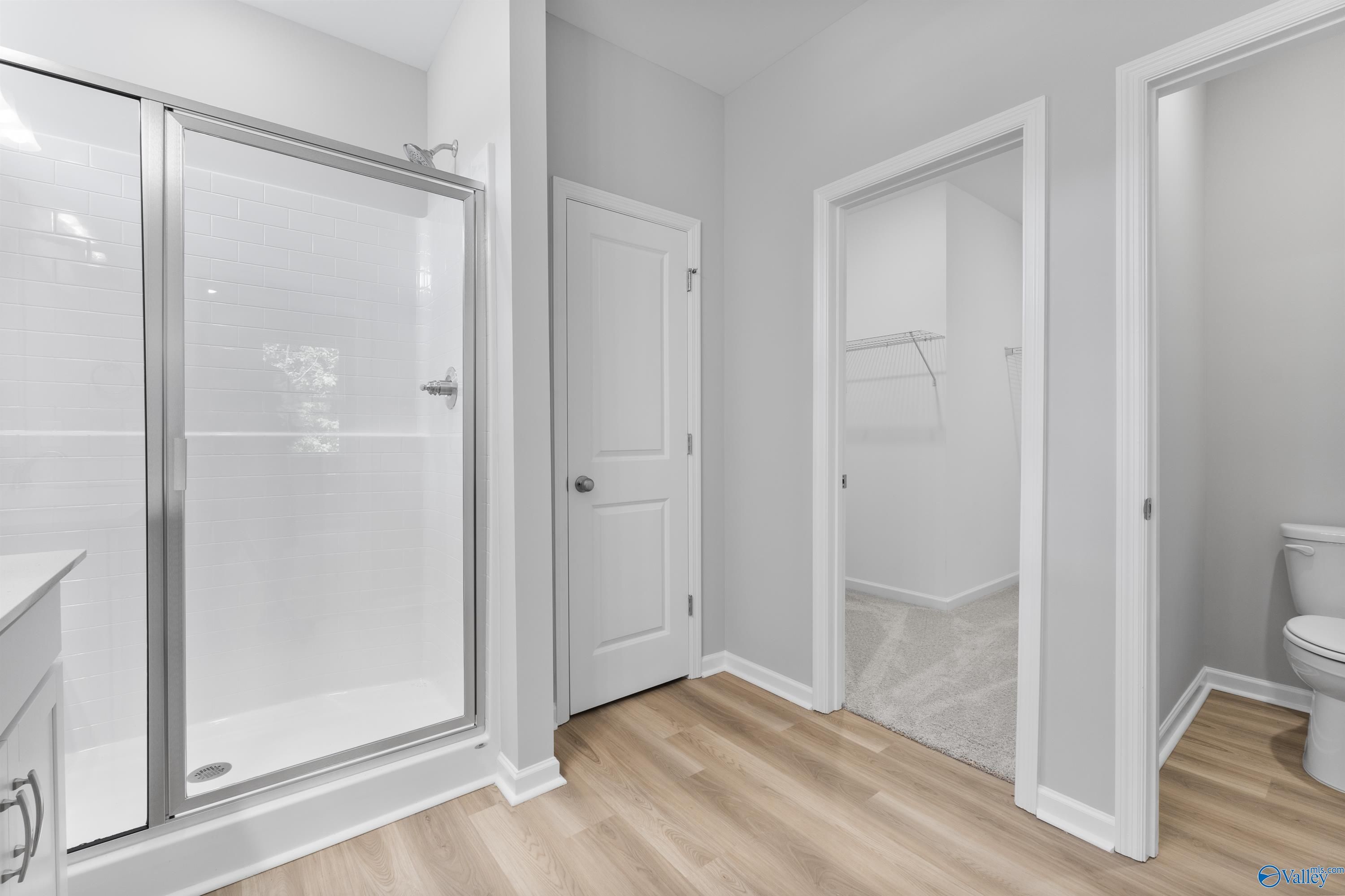 Modern master bathroom featuring frameless glass shower, white vanity, and walk-in closet access in Davidson Homes The Phoenix, Hazel Green, AL