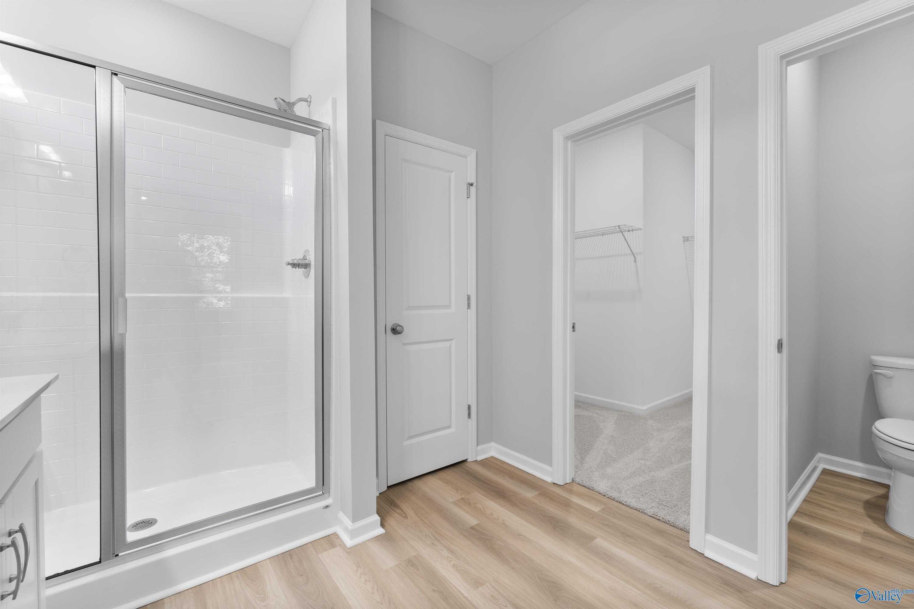 Modern master bathroom featuring frameless glass shower, white vanity, and walk-in closet access in Davidson Homes The Phoenix, Hazel Green, AL