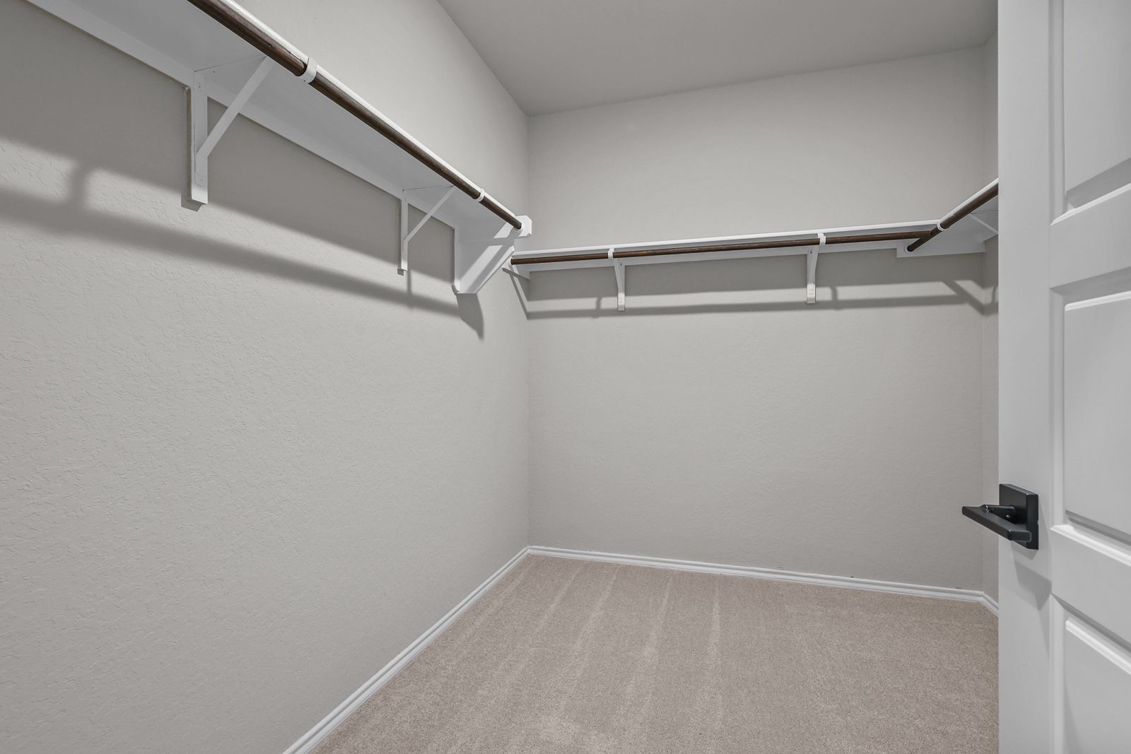 Spacious walk-in closet in The Glenwood master suite featuring neutral carpeting and built-in shelving.