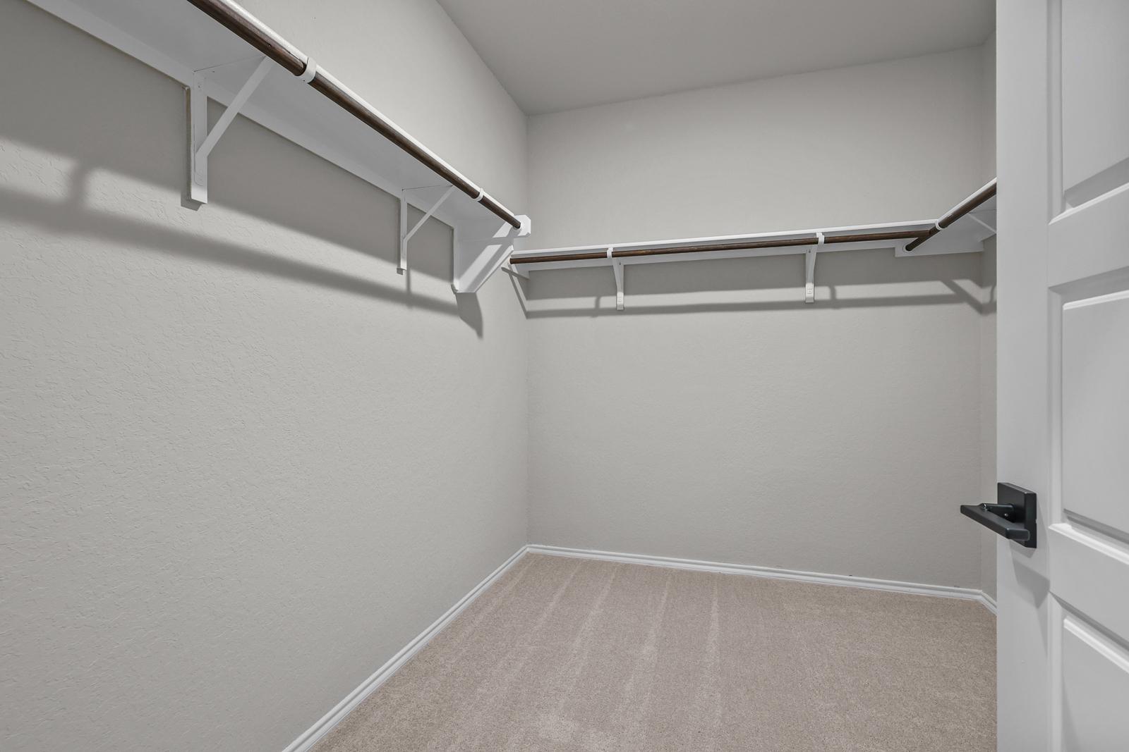 Spacious walk-in closet in The Glenwood master suite featuring neutral carpeting and built-in shelving.