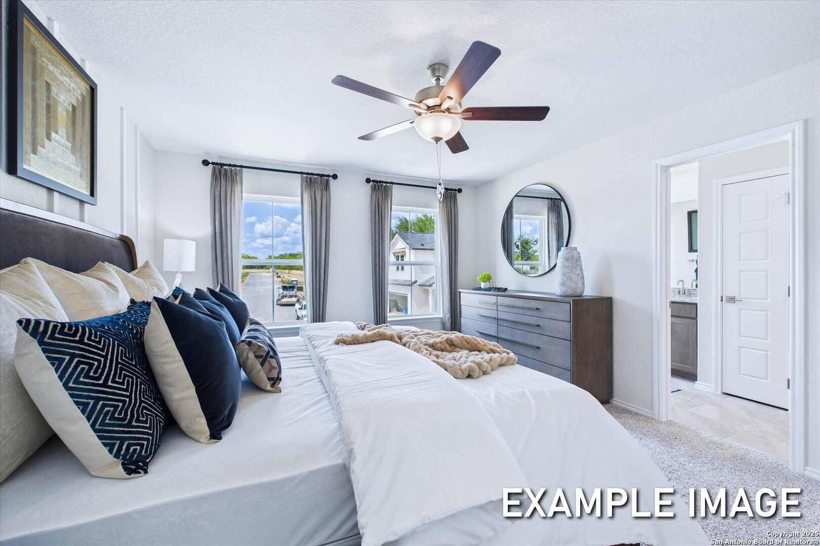 Elegant master bedroom with king bed, plush pillows, ceiling fan, and large windows in Davidson Homes The Gillian B, San Antonio