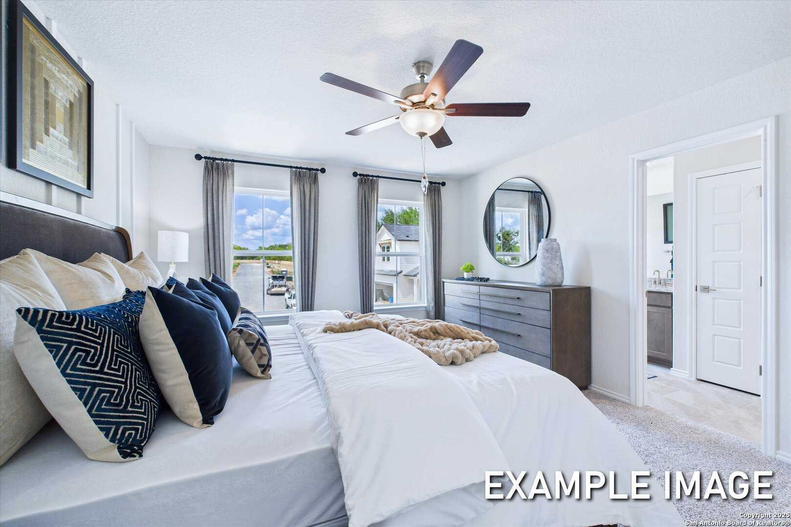 Elegant master bedroom with king bed, plush pillows, ceiling fan, and large windows in Davidson Homes The Gillian B, San Antonio