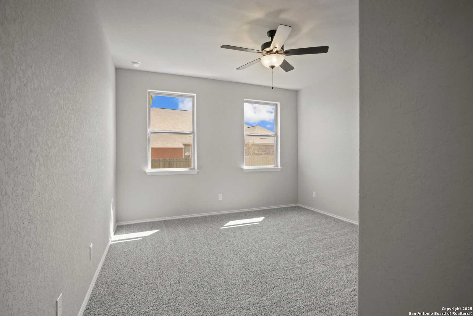 Bright secondary bedroom featuring ceiling fan, large windows with natural light, and neutral carpet in Davidson Homes The Asheville E, Converse, Texas