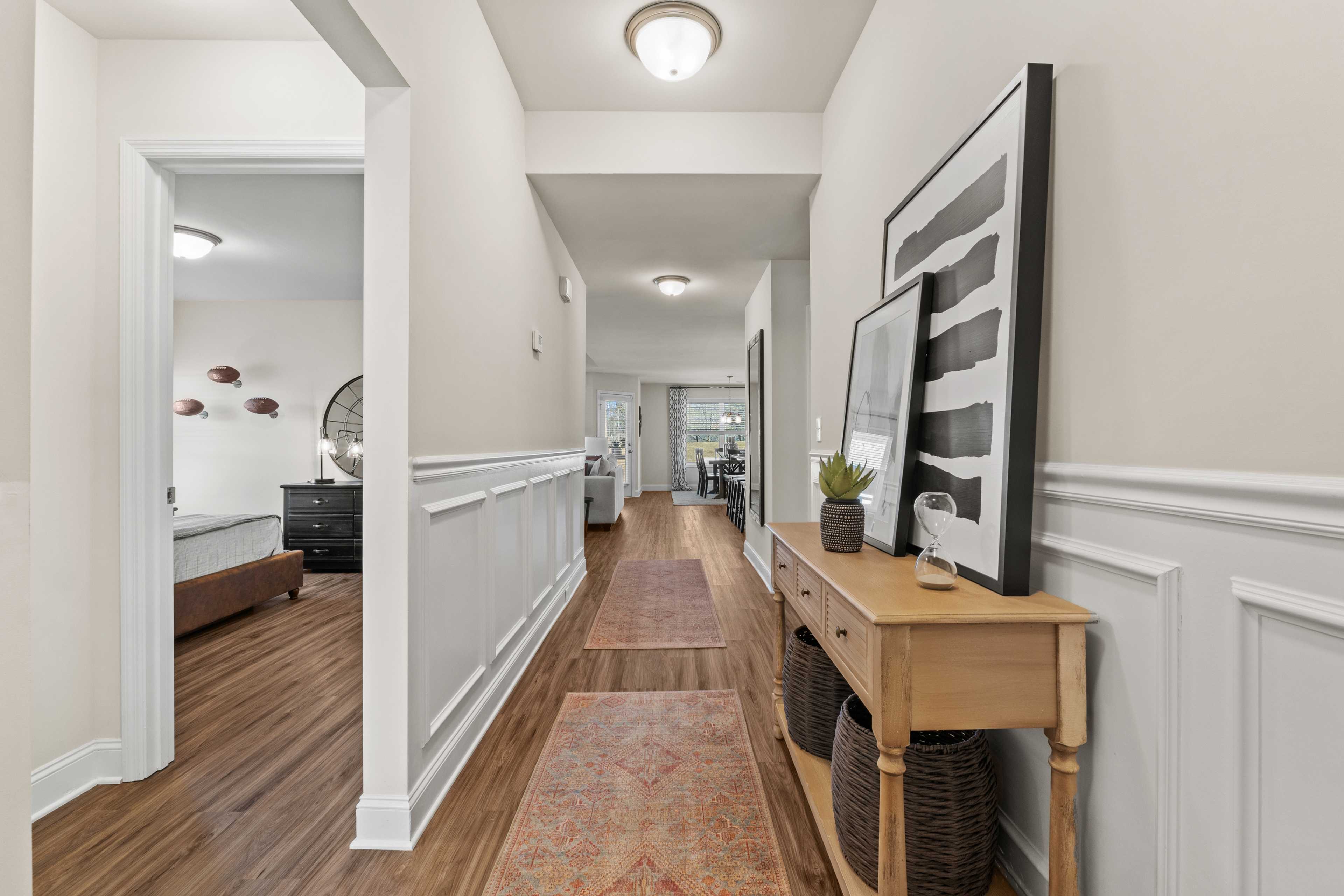 Elegant hallway with wainscoting, hardwood floors, and runner rug at Ramsay Cove in Owens Cross Roads AL featuring console table and abstract wall art
