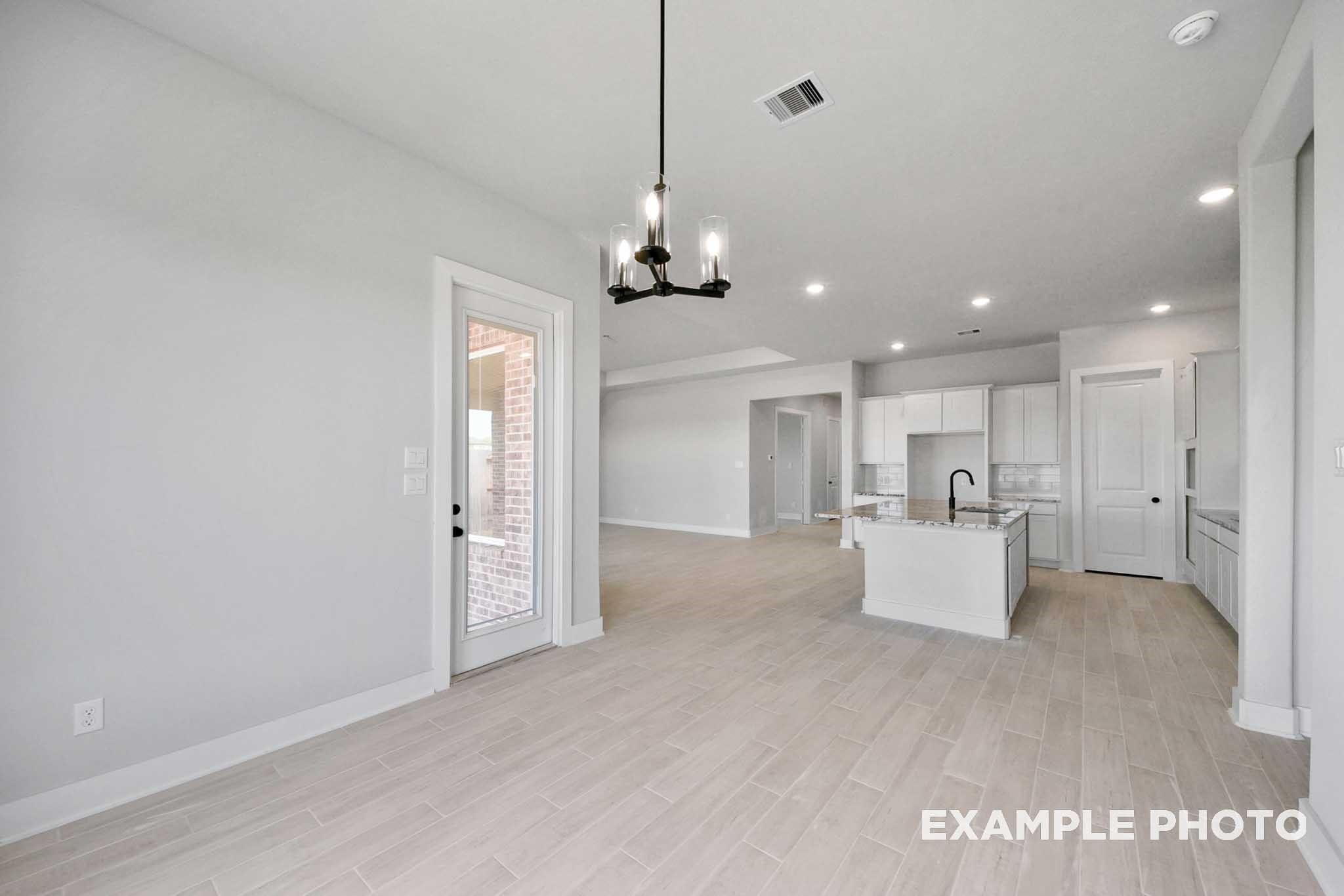 Open-concept kitchen with white island sink and cabinets, dining area with chandelier and French doors in Davidson Homes The George A, Lago Mar
