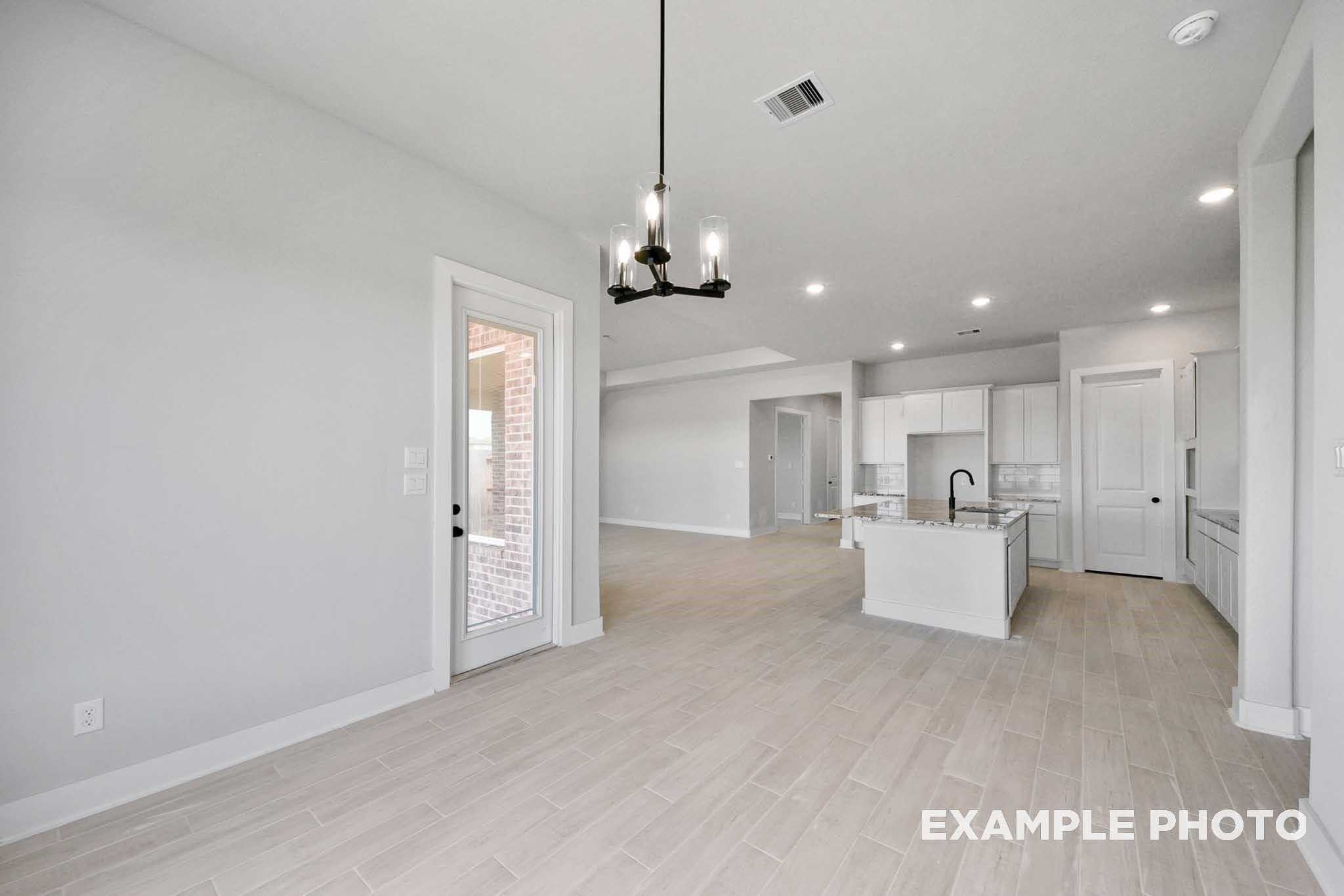 Open-concept kitchen with white island sink and cabinets, dining area with chandelier and French doors in Davidson Homes The George A, Lago Mar