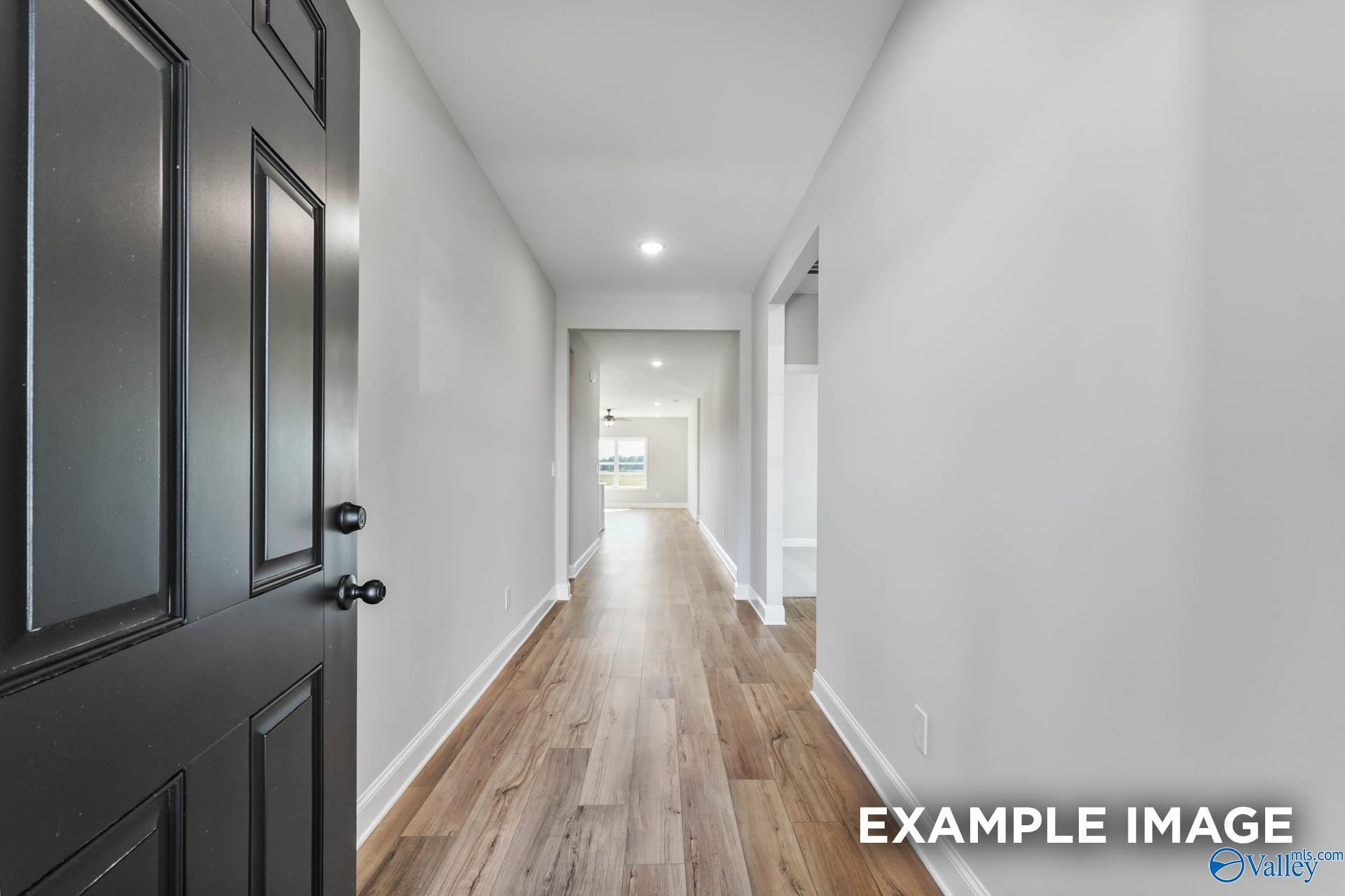 Long entry hallway with hardwood floors, white walls, and open black door in Davidson Homes The Daphne C, Athens, Alabama