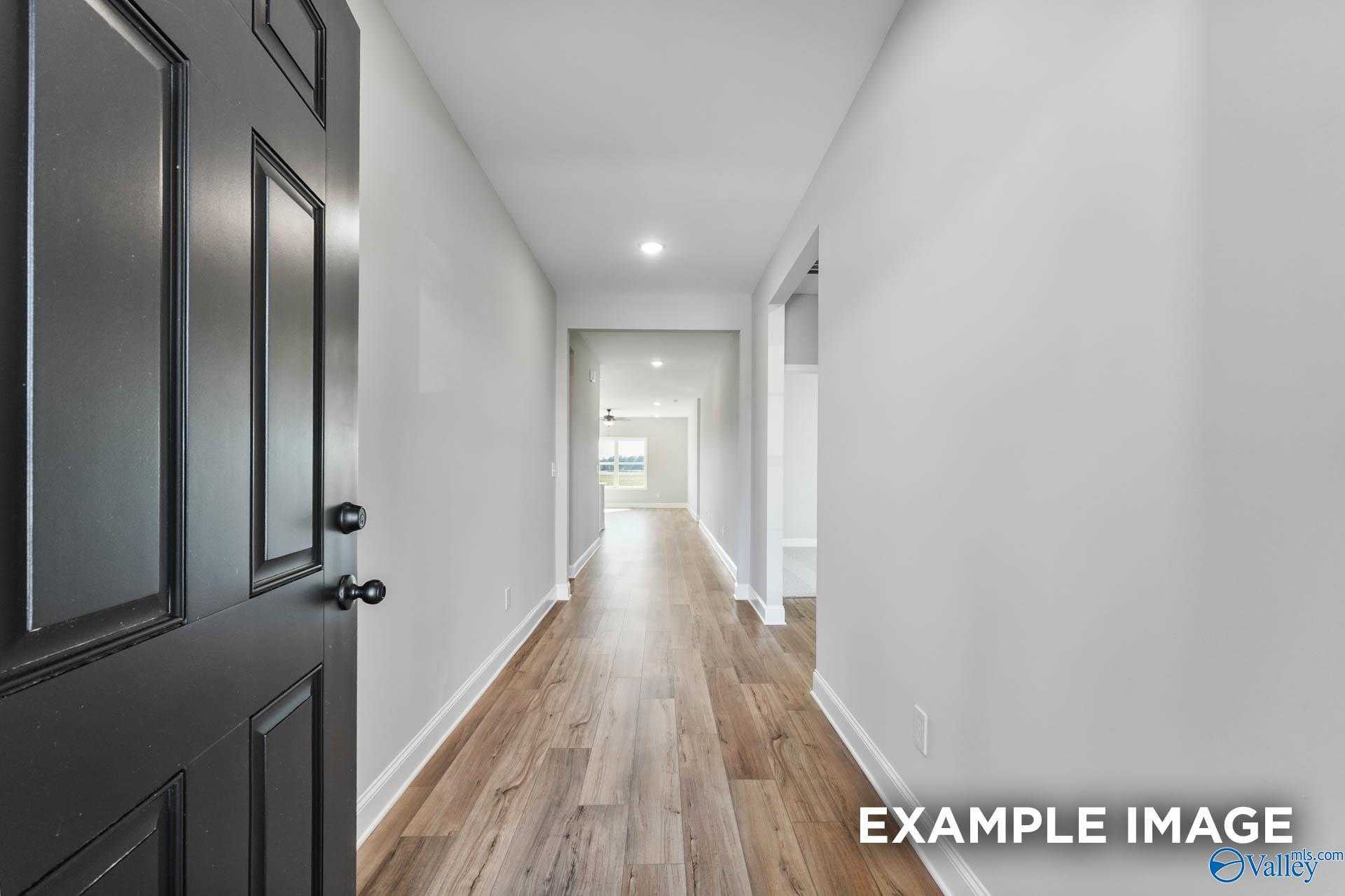 Long entry hallway with hardwood floors, white walls, and open black door in Davidson Homes The Daphne C, Athens, Alabama