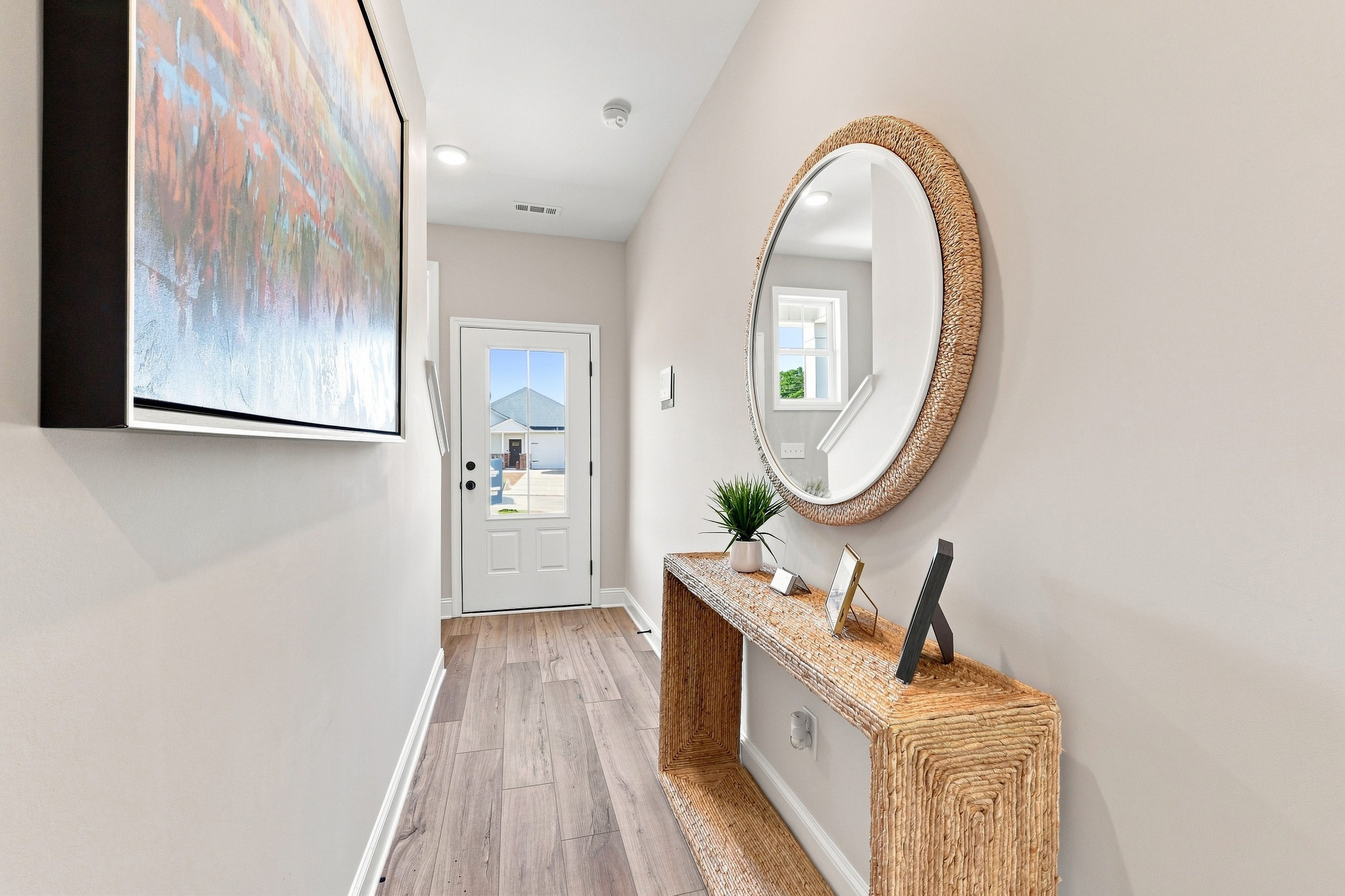 Bright foyer entry at Bailey Park by Davidson Homes in Fayetteville TN with rattan console table, round mirror, and glass-panel front door