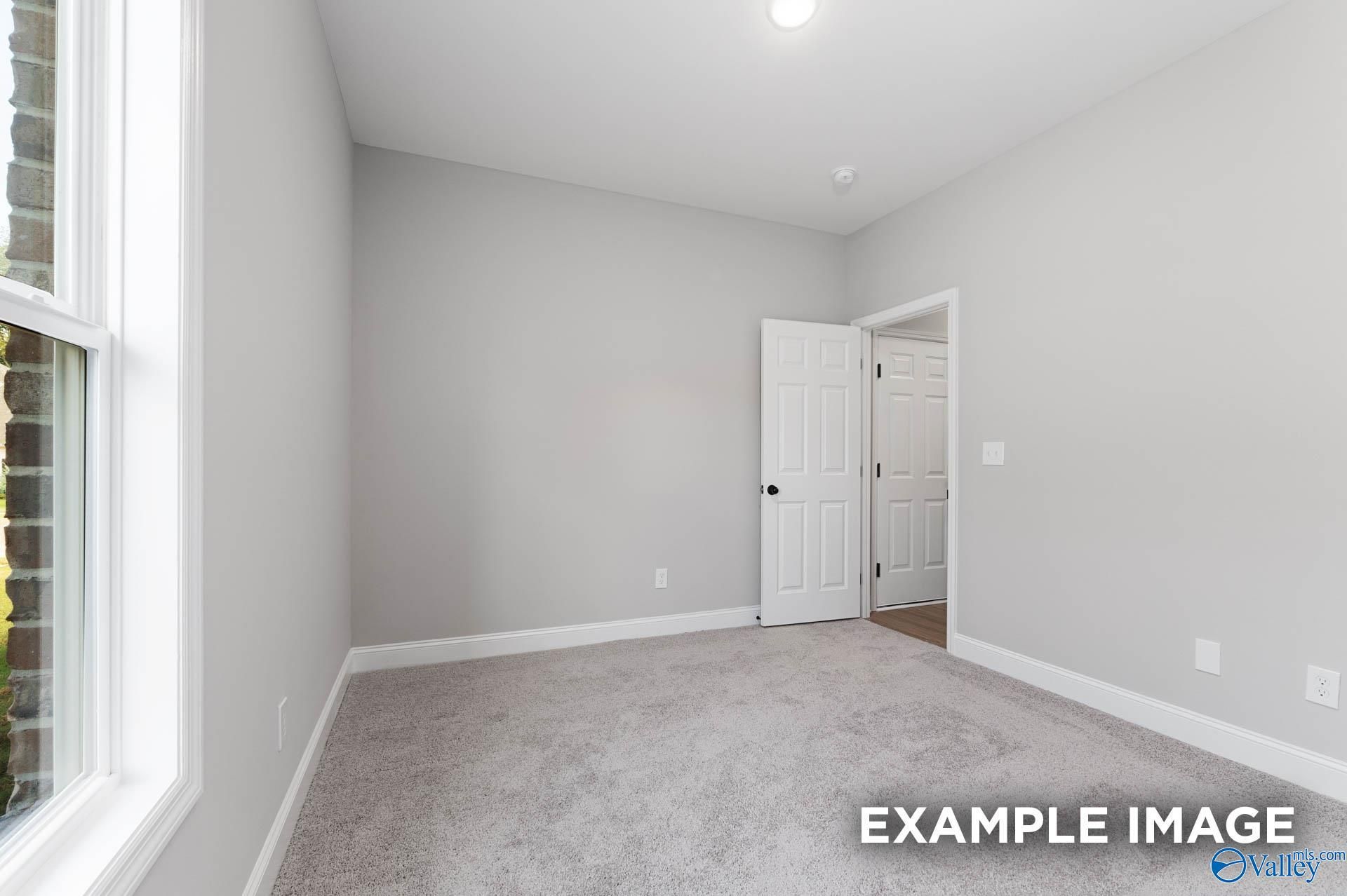 Spacious empty bedroom with gray walls, carpet floor, large window, and adjacent door in Davidson Homes The Daphne D, Meridianville, AL
