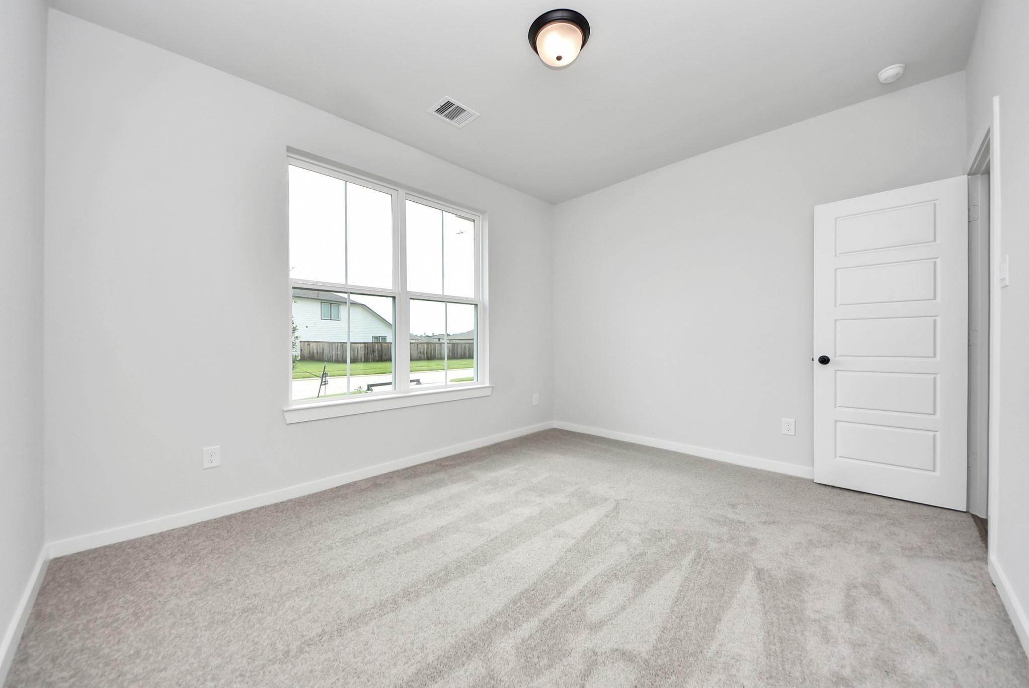 Bright, carpeted bedroom with large window in The Daphne F floor plan by Davidson Homes in Sundance Cove, Crosby, Texas.