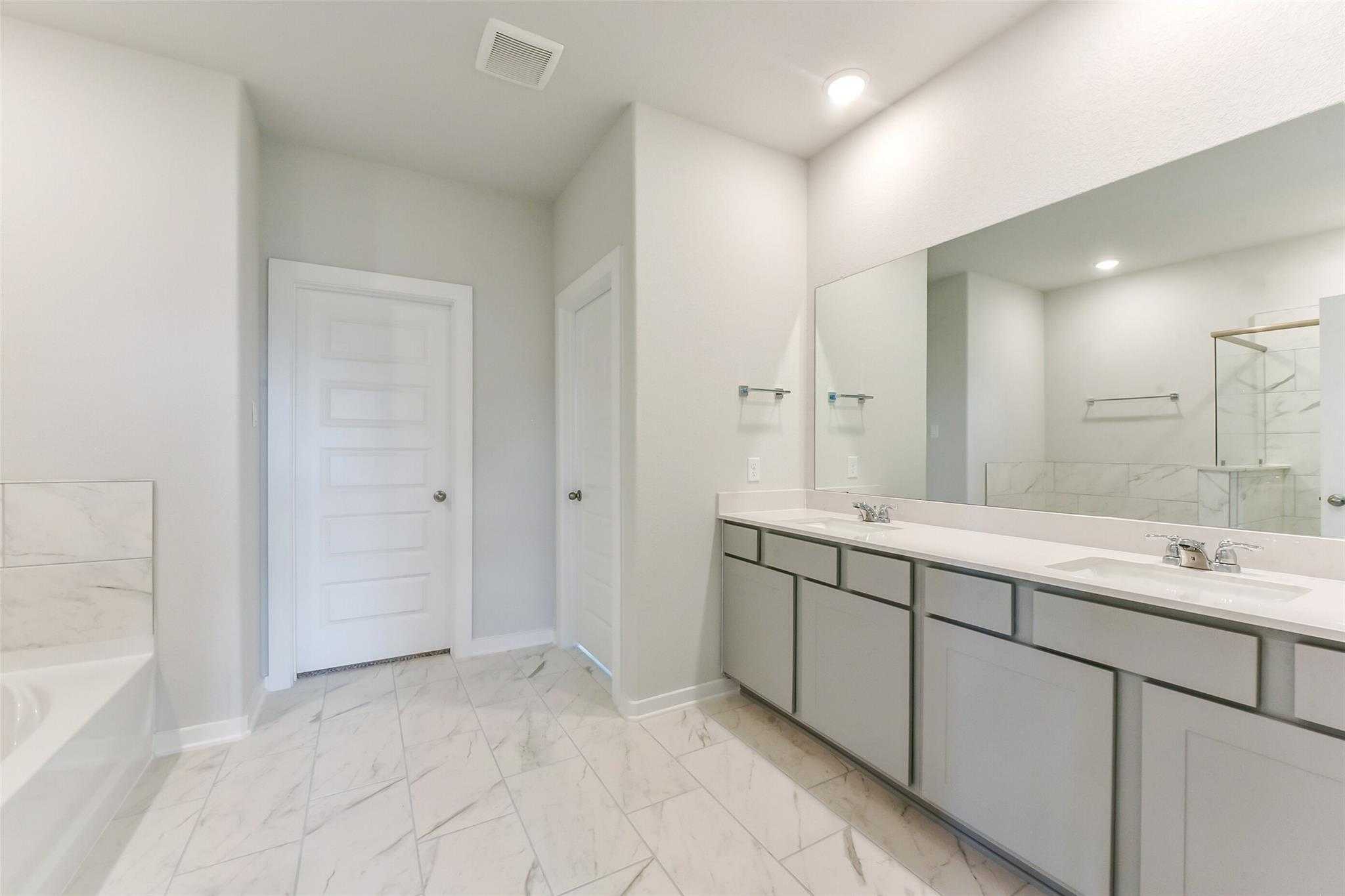 Modern master bathroom featuring double vanity, subway tile backsplash, and freestanding tub in Davidson Homes The Laguna C, Rosharon, Texas