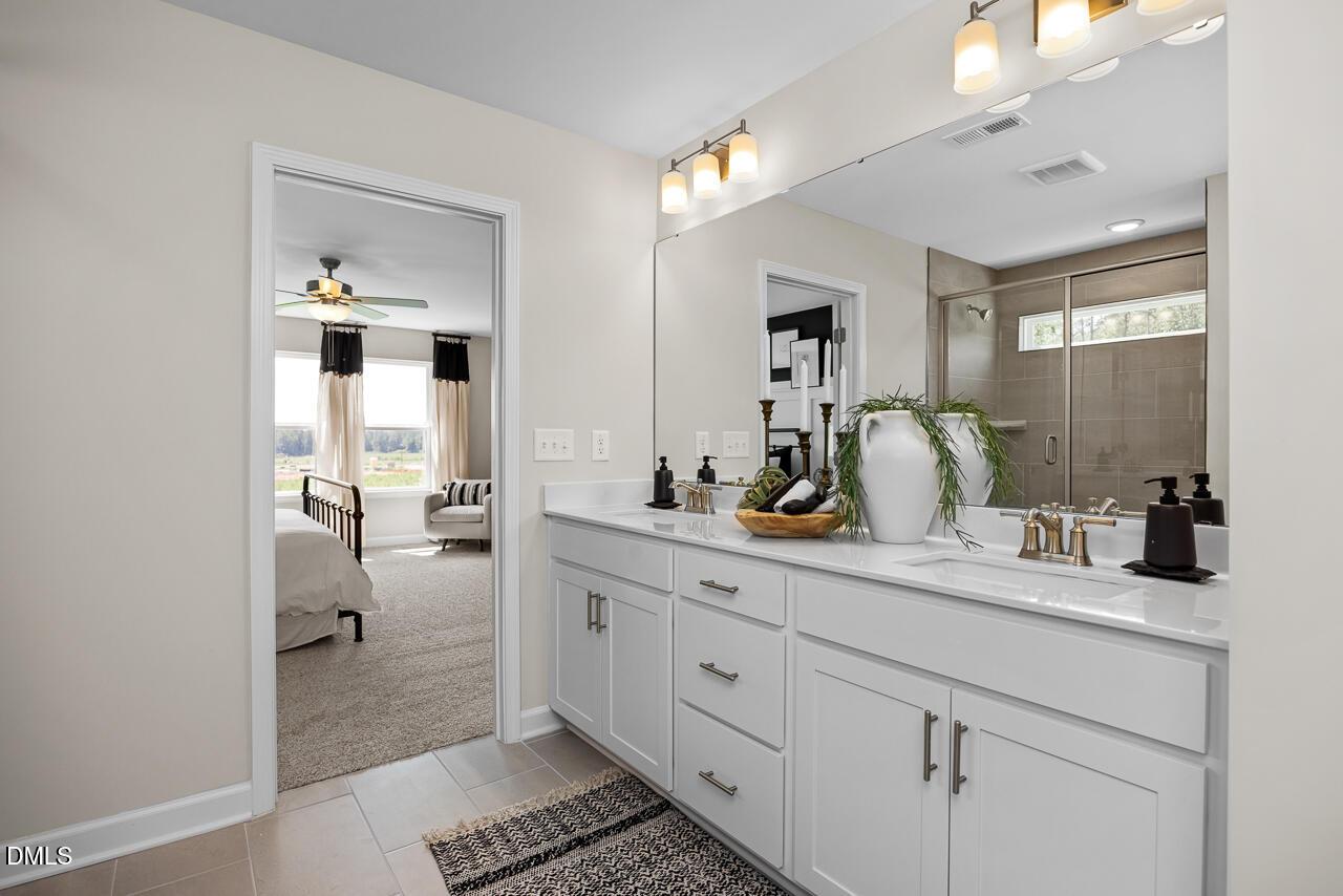 Elegant master bathroom with double vanity, greenery accents, and bedroom view in Davidson Homes The Hickory II C, Zebulon, NC