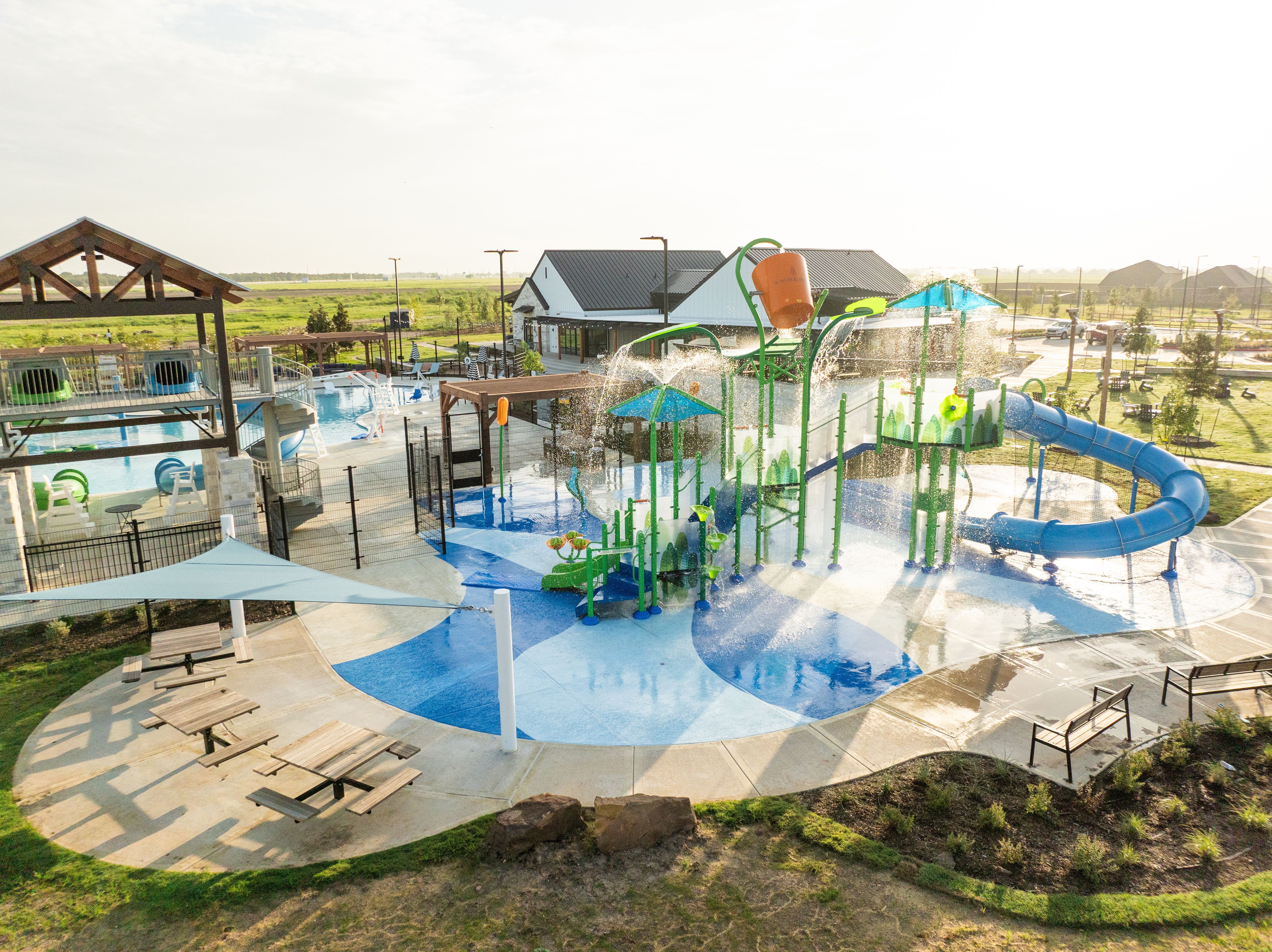 Vibrant splash pad at Emberly in Beasley Texas featuring green climbing structures blue slides and shaded lounge seating