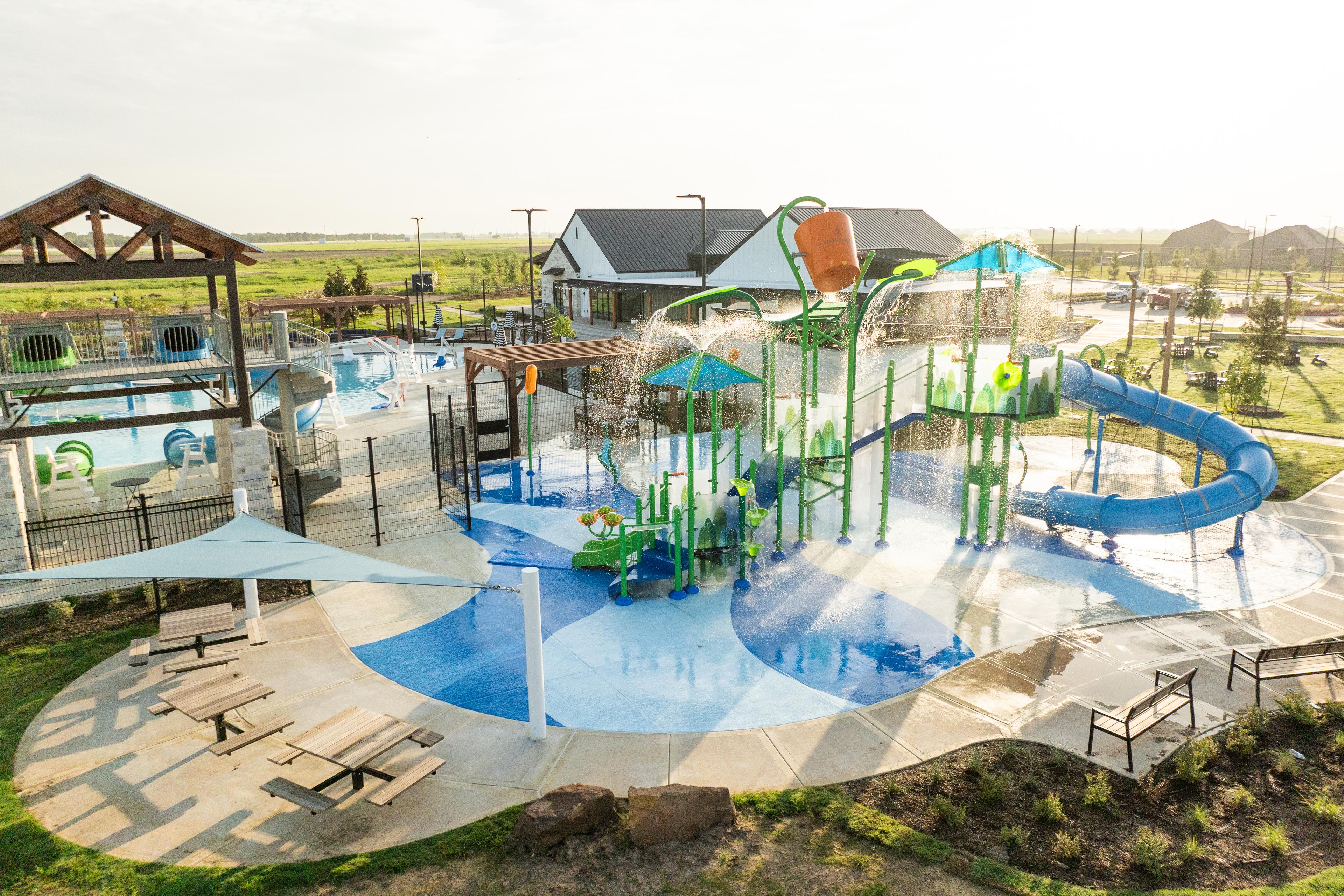 Vibrant splash pad at Emberly in Beasley Texas featuring green climbing structures blue slides and shaded lounge seating