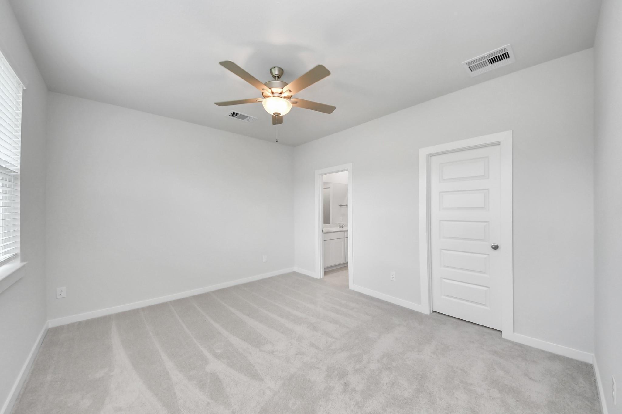 Bright secondary bedroom with plush carpet and ceiling fan in The Frio F floor plan at Liberty Estates, Cleveland, Texas.