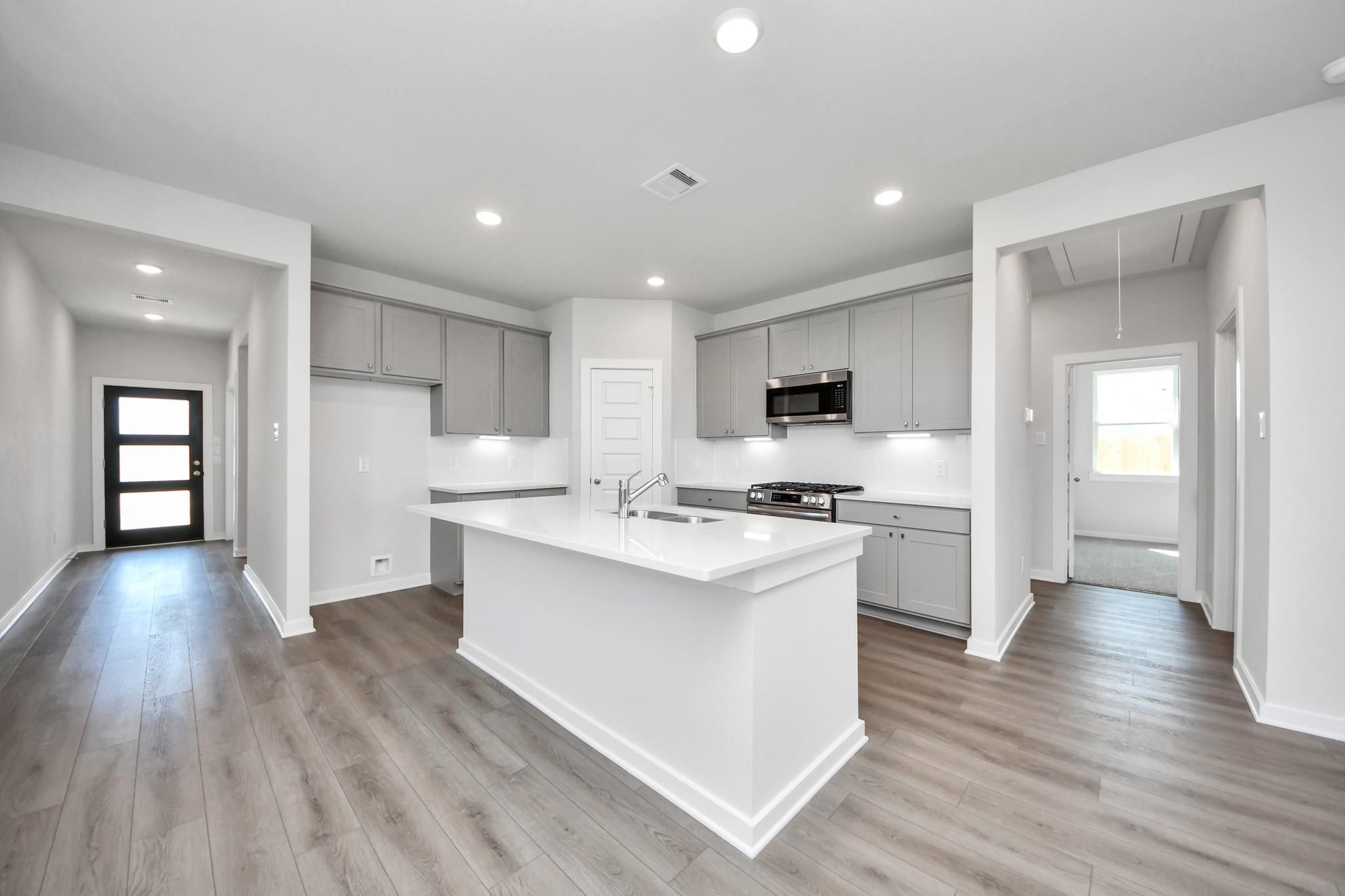 Modern kitchen with white island, grey cabinets, and stainless appliances in The Riviera A plan at Emberly, Beasley, TX.