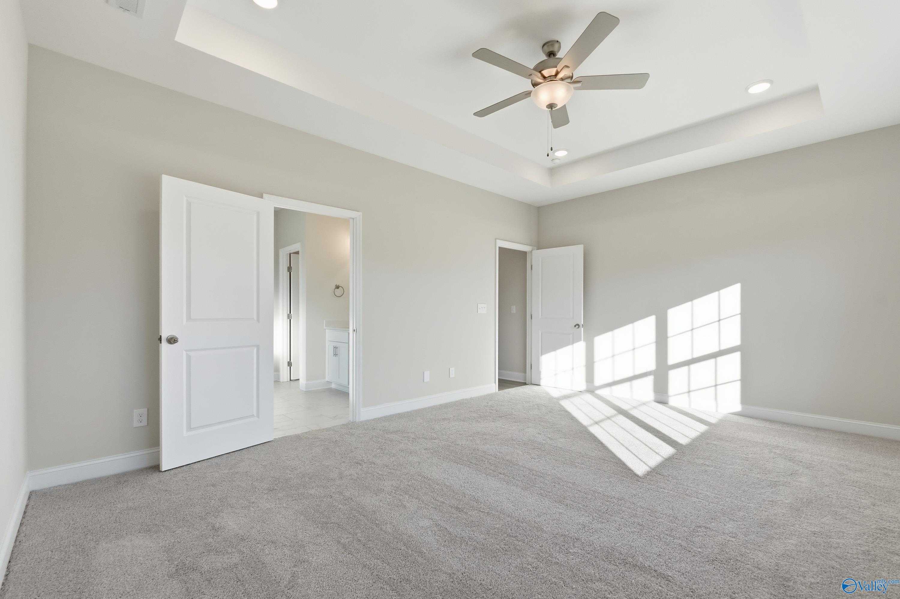 Spacious bedroom with beige walls, gray carpet, ceiling fan, and open doors to bath in Davidson Homes Montgomery B, Toney, AL