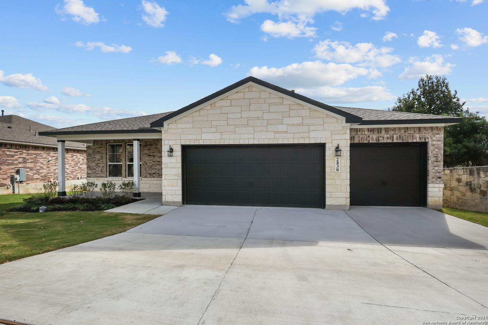 Modern 1-story home with beige stone-brick facade, 3-car black garage, driveway, and landscaped yard in Ladera, San Antonio, Texas