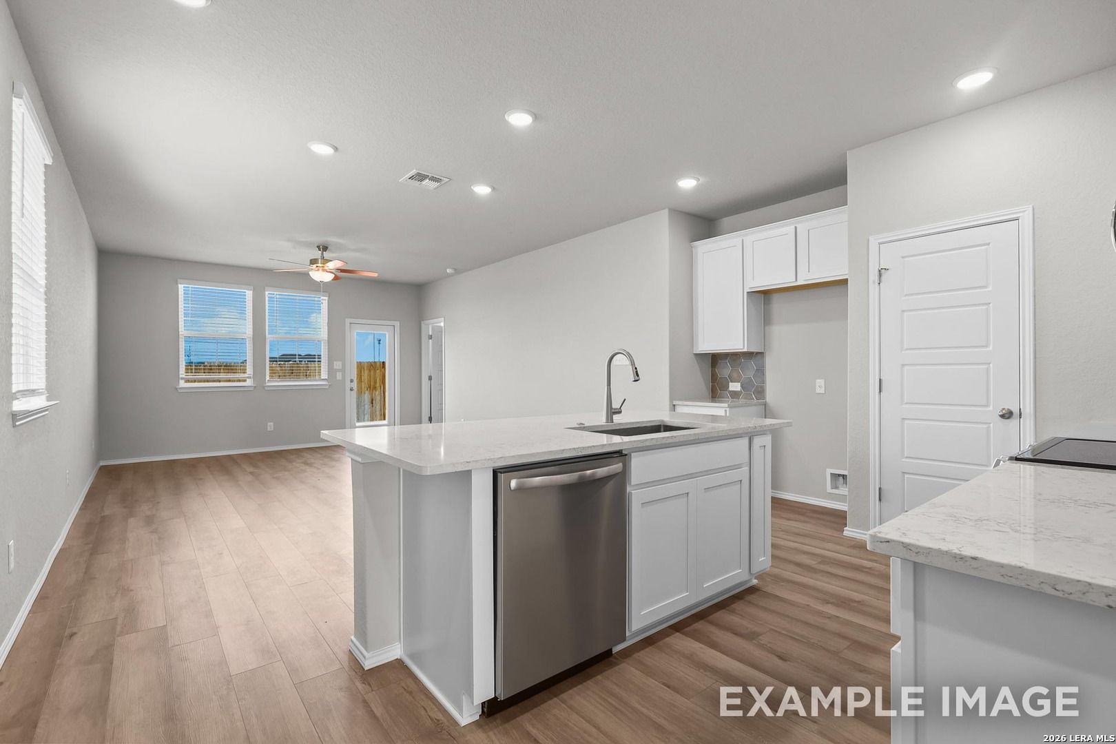 Bright open-concept kitchen with white island, stainless dishwasher, sink, and hardwood floors in Davidson Homes The Colorado D, San Antonio