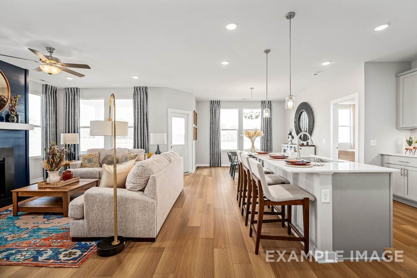 Open-concept living room with beige sofa, gold lamp, and white kitchen island in Davidson Homes The Franklin B, Sage Farms, White House, Tennessee