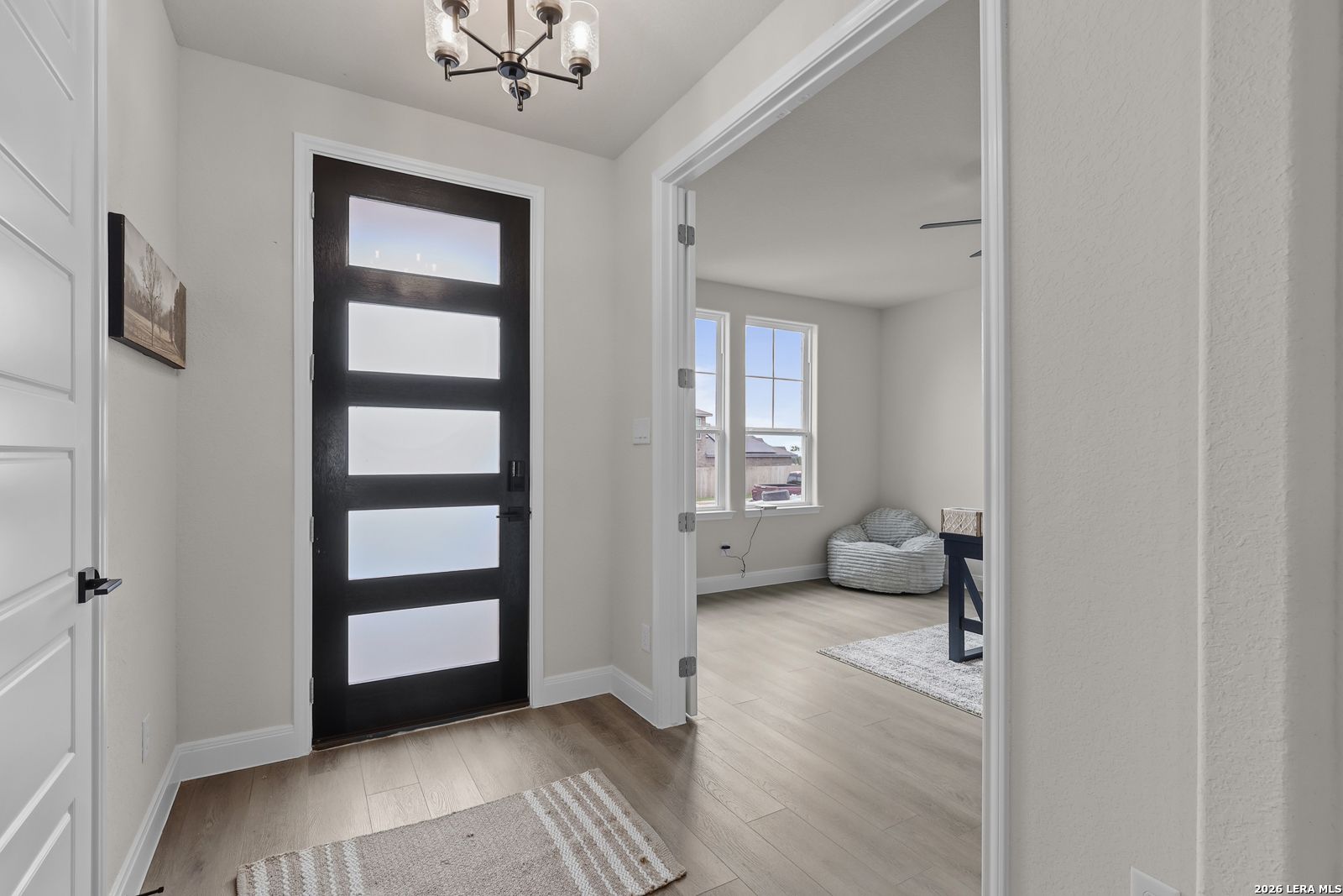 Modern entryway featuring black frosted glass door, chandelier, and open living space in Davidson Homes The Lanier G, Castroville, Texas