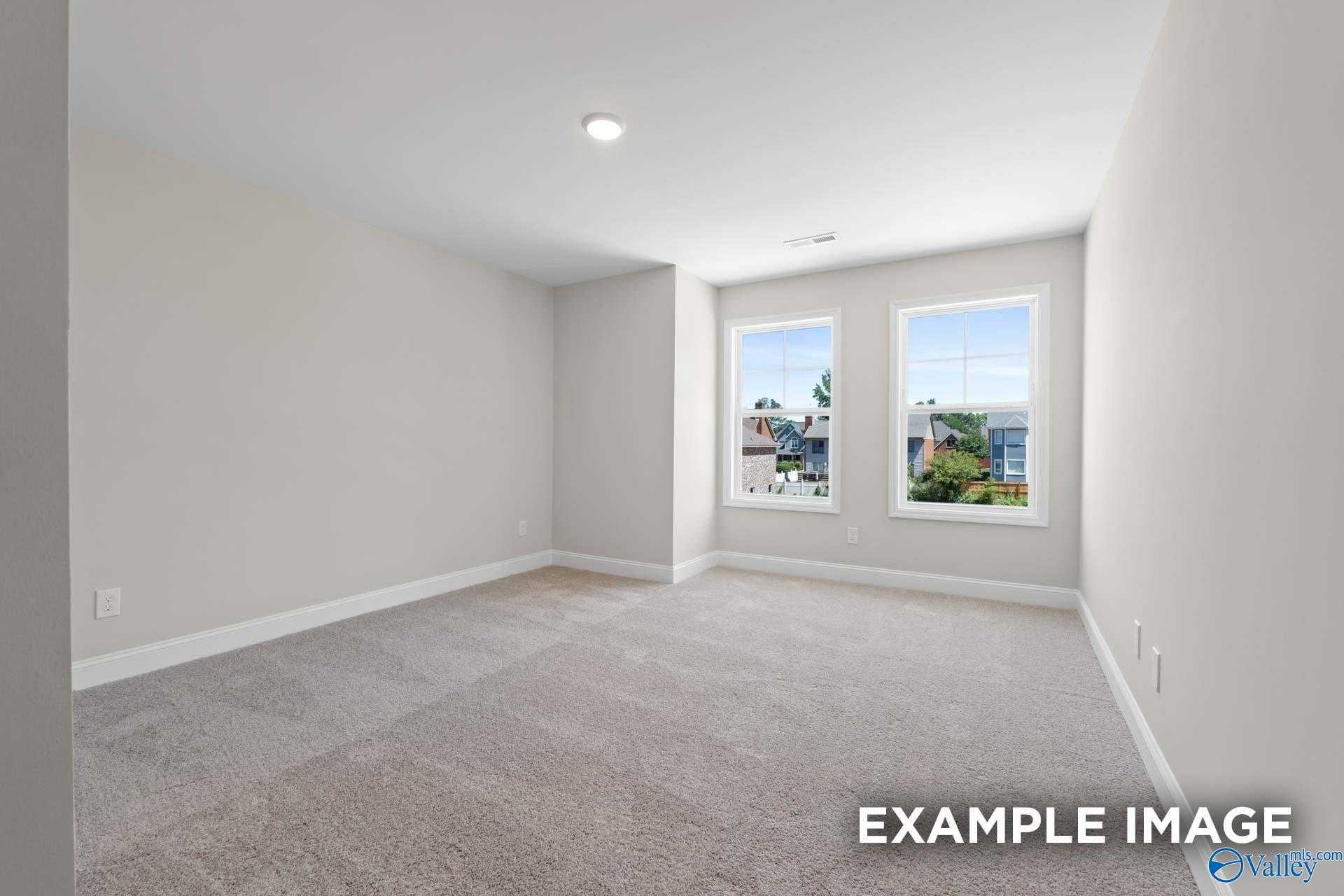 Spacious empty bedroom with neutral gray walls, beige carpet, and large windows overlooking trees in Davidson Homes The Camden C, Huntsville, AL