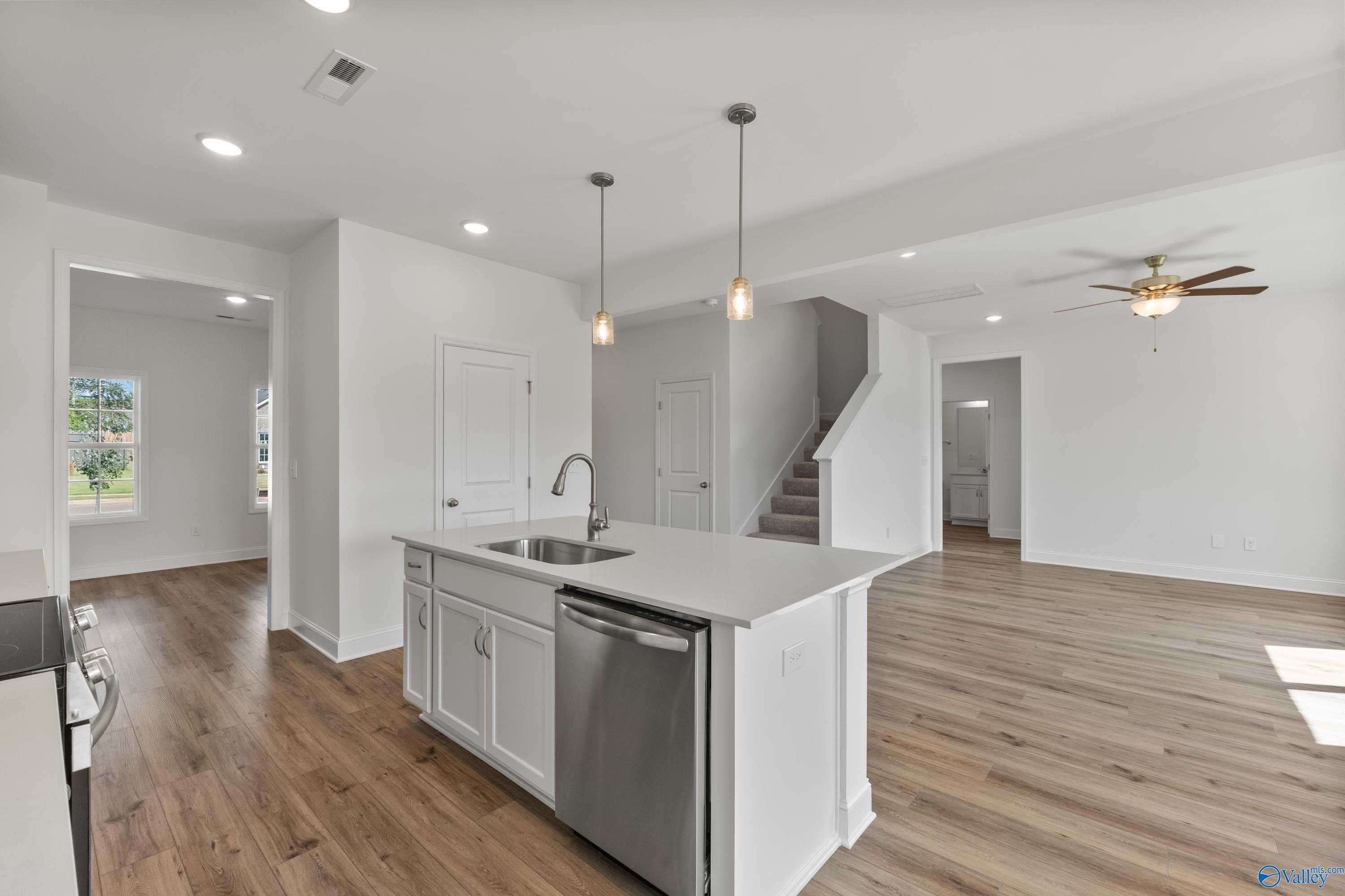 Modern open-concept kitchen with white island, stainless sink, pendant lights, and hardwood floors in Davidson Homes The Shelby A, New Market, Alabama