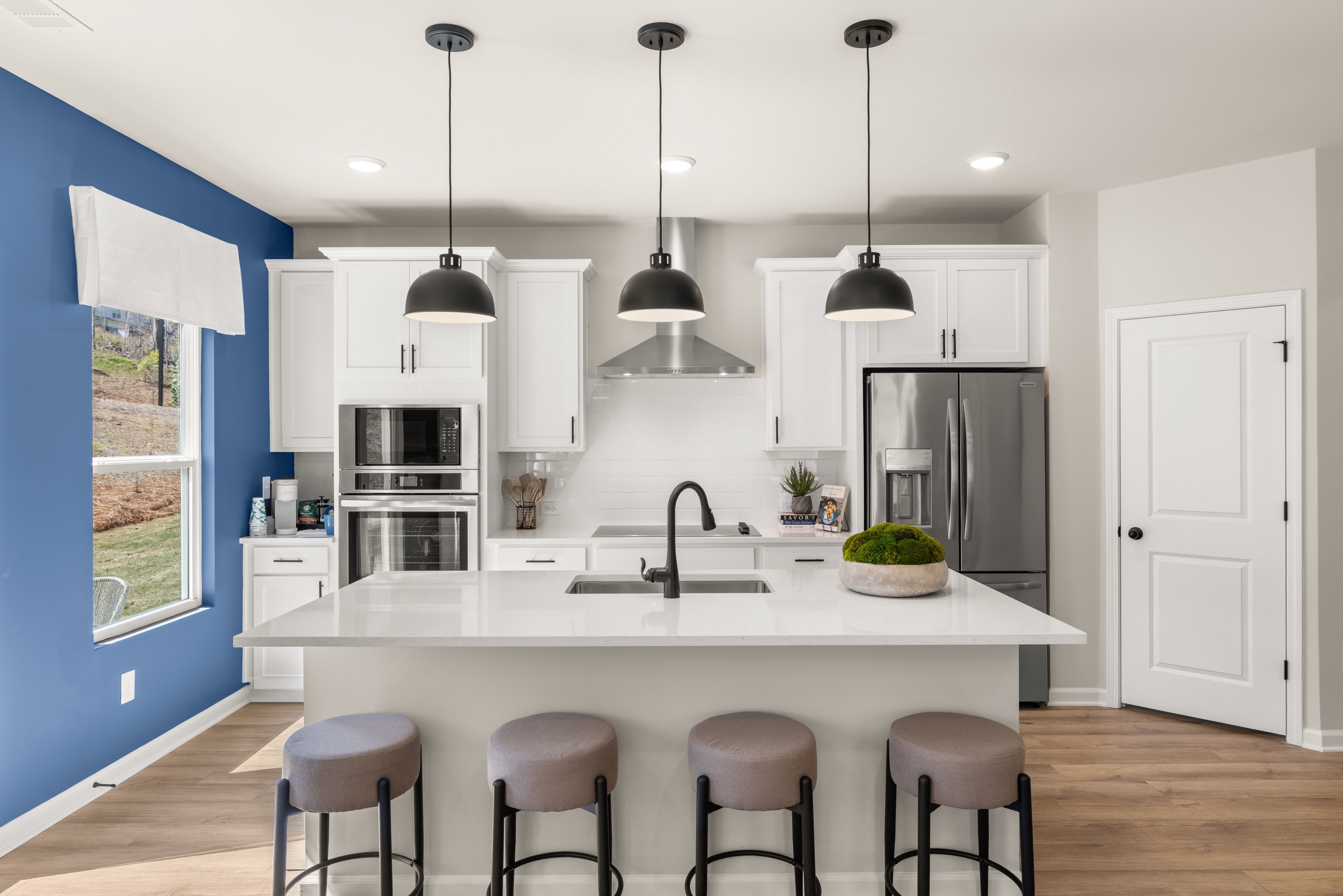 Modern kitchen at The Bluffs in Canton GA with white island, blue accent wall, pendant lights, and stainless appliances