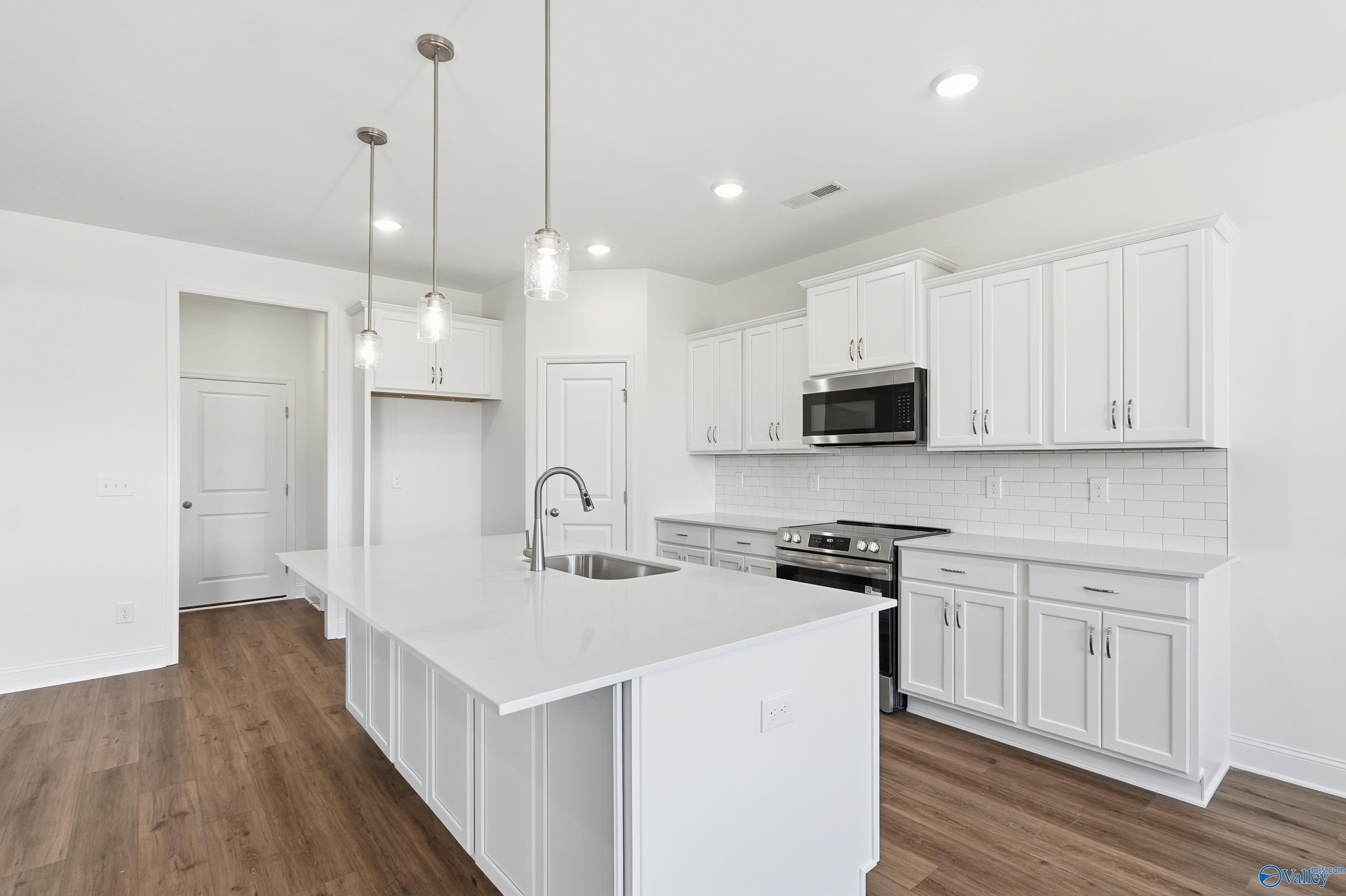 Bright modern kitchen with white cabinets, large island sink, stainless appliances, and pendant lights in Davidson Homes The Montgomery, Meridianville AL