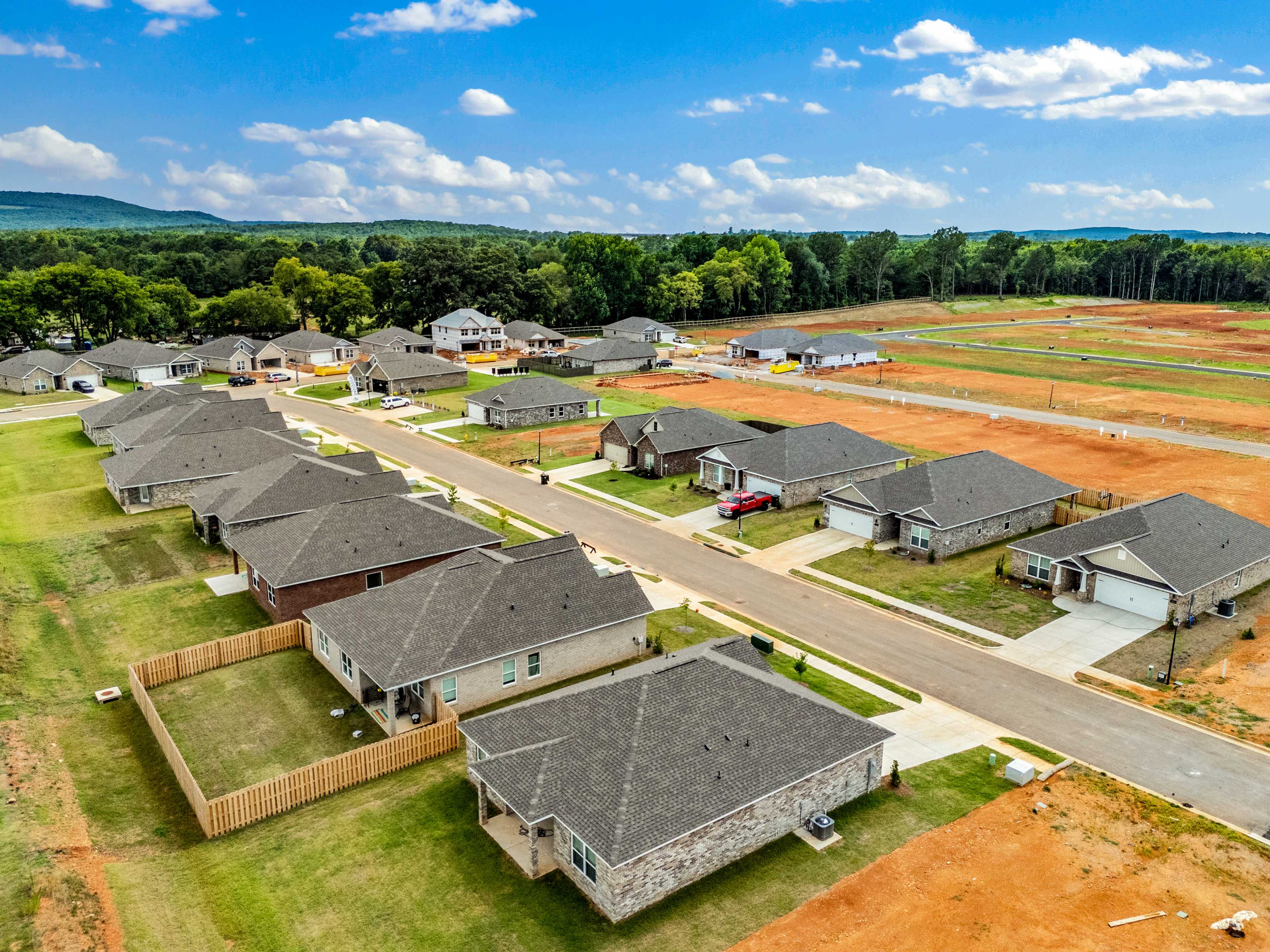 Aerial view of Wood Trail neighborhood in Toney Alabama with new Davidson Homes, shingled roofs, green lawns, red dirt lots, and wooded hills