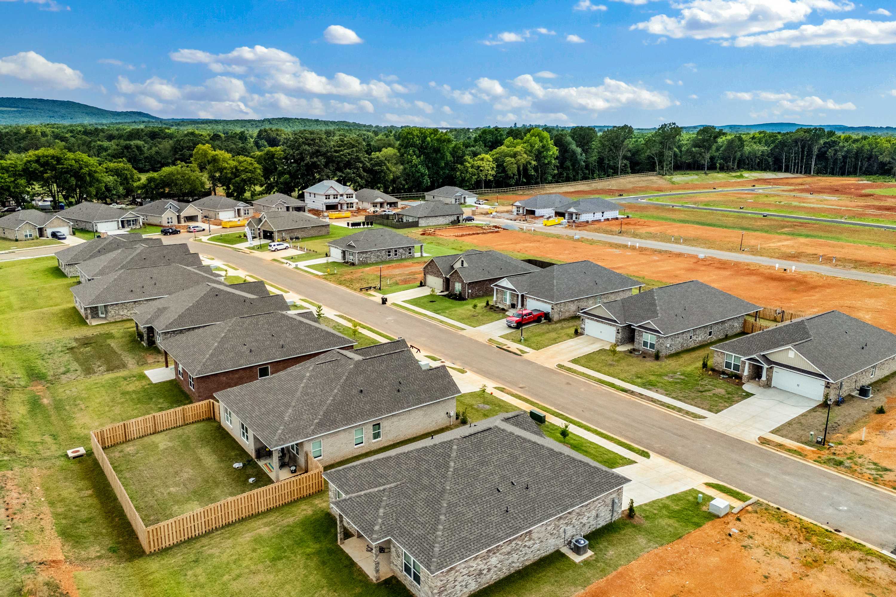 Aerial view of new homes in Wood Trail Toney Alabama by Davidson Homes with brick facades, green lawns, and wooded hills under blue sky