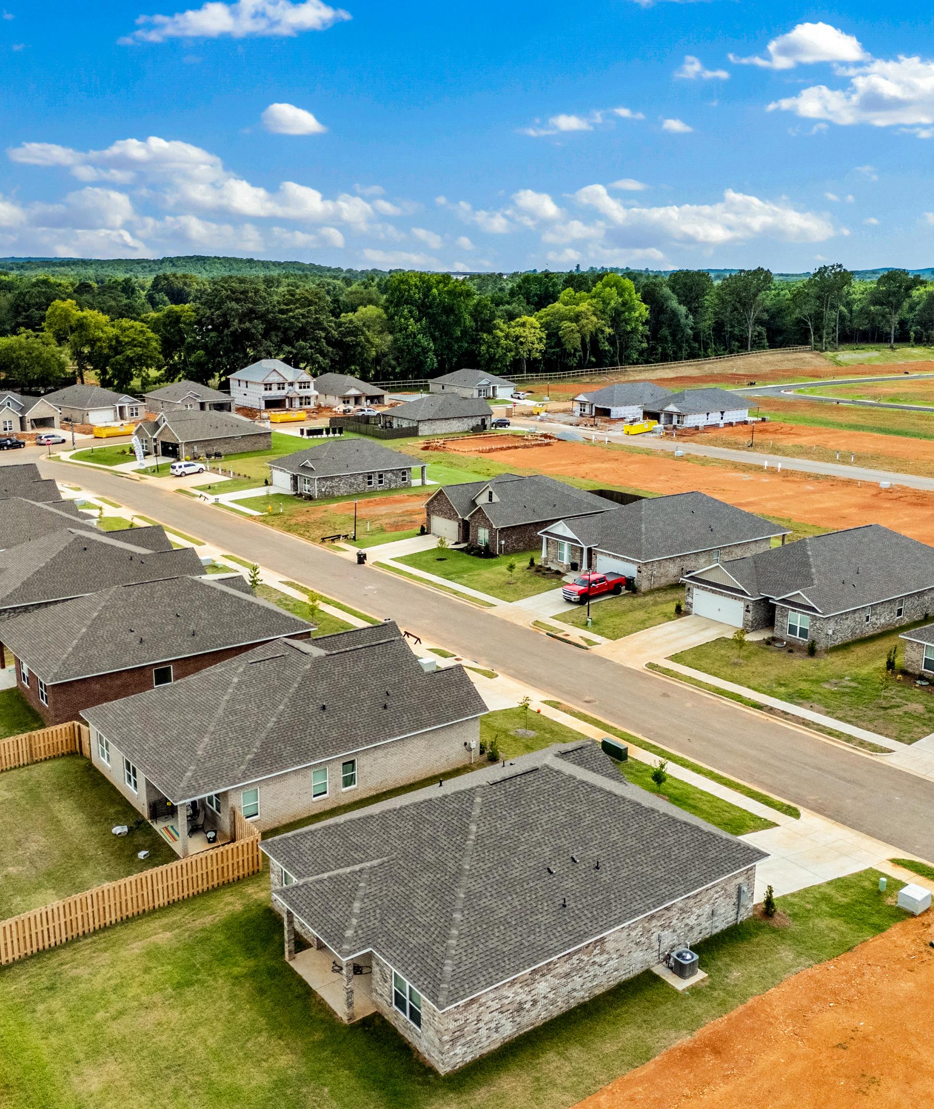 Aerial view of Wood Trail neighborhood in Toney Alabama with new Davidson Homes, shingled roofs, green lawns, red dirt lots, and wooded hills