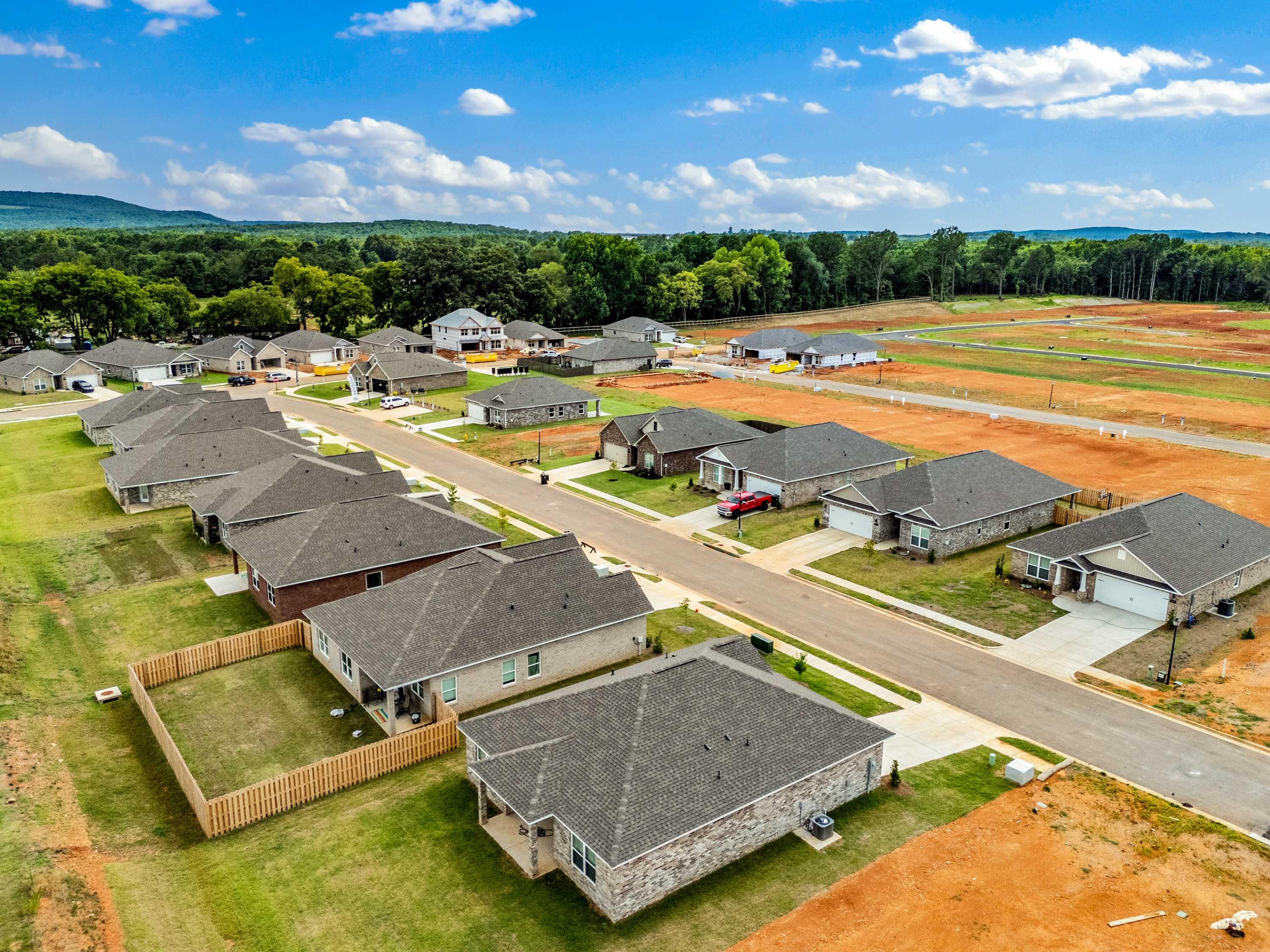 Aerial view of Wood Trail neighborhood in Toney Alabama with new Davidson Homes, shingled roofs, green lawns, red dirt lots, and wooded hills
