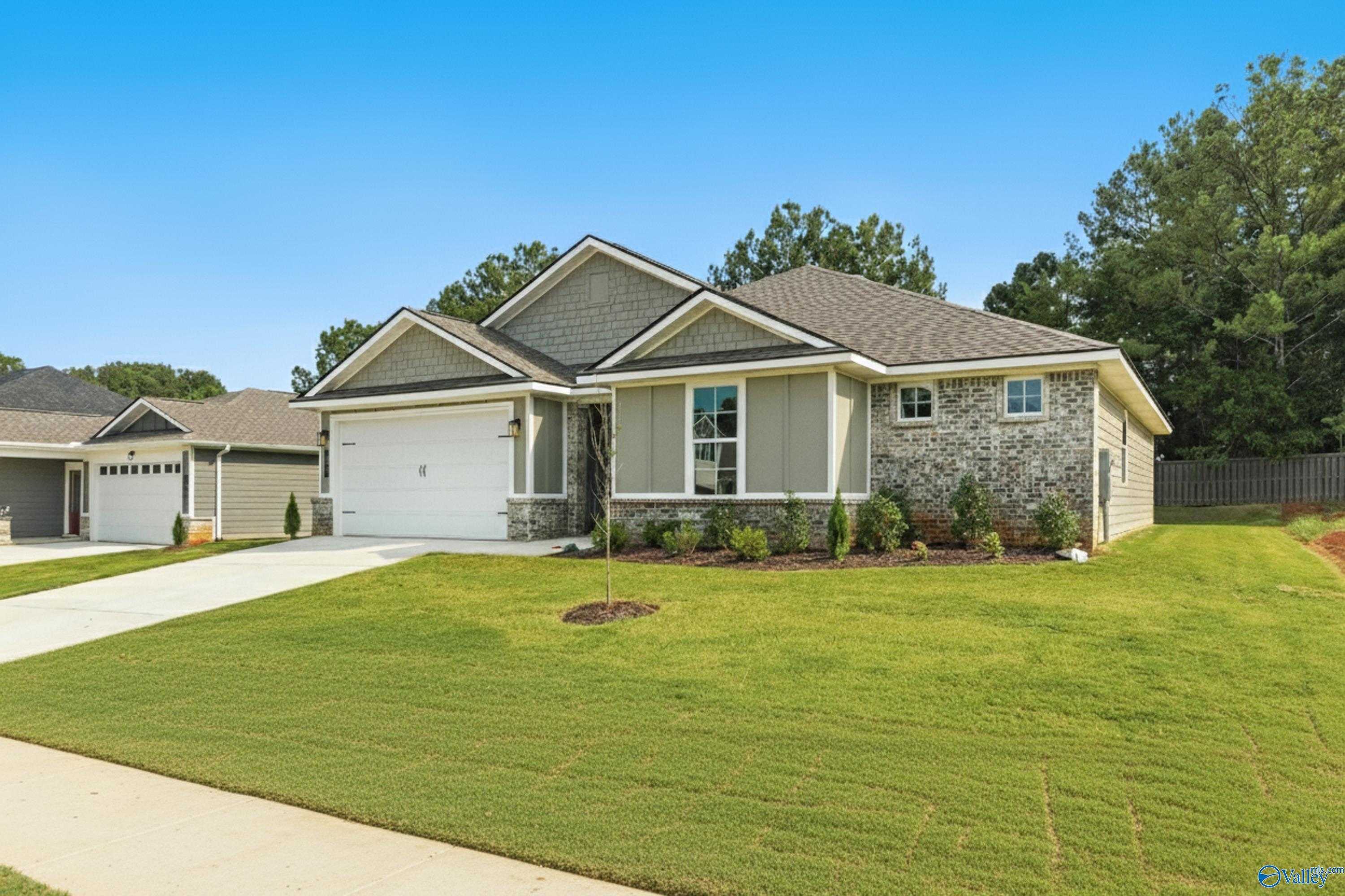 Modern gray single-story home with 2-car garage, lush green lawn, and trees in Evergreen Mill, Madison, Alabama by Evermore Homes The Grace