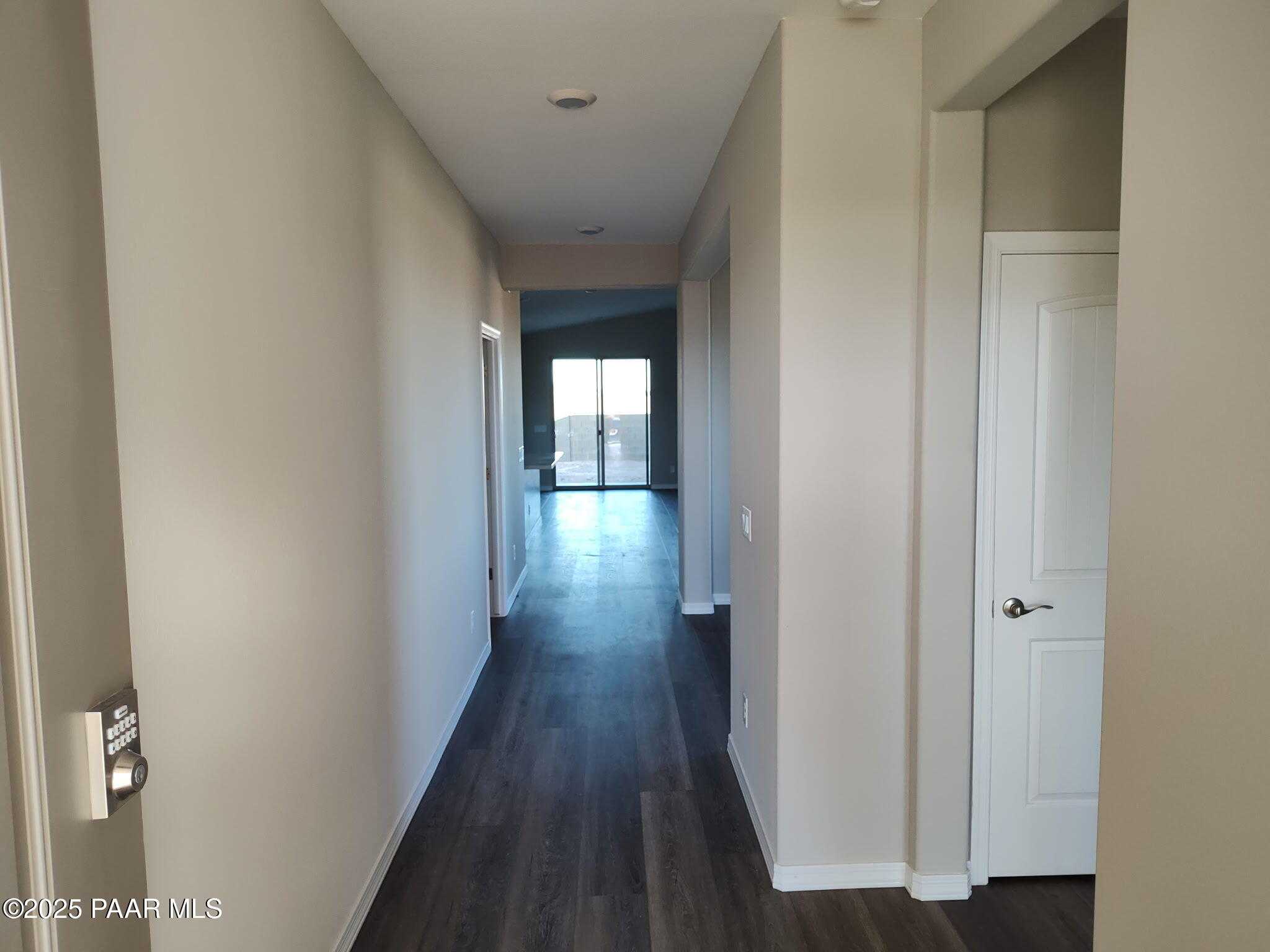 Long hallway with beige walls, dark hardwood floors, and sliding glass doors to patio in Davidson Homes The Frontier A, Prescott Valley, AZ
