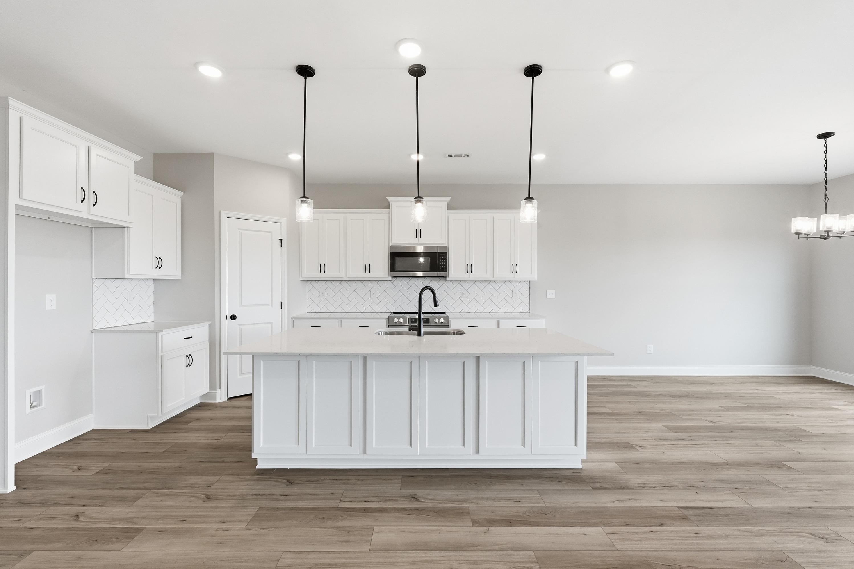 Spacious white kitchen in The Rockford plan featuring large center island, shaker cabinets, subway tile backsplash, and pendant lights