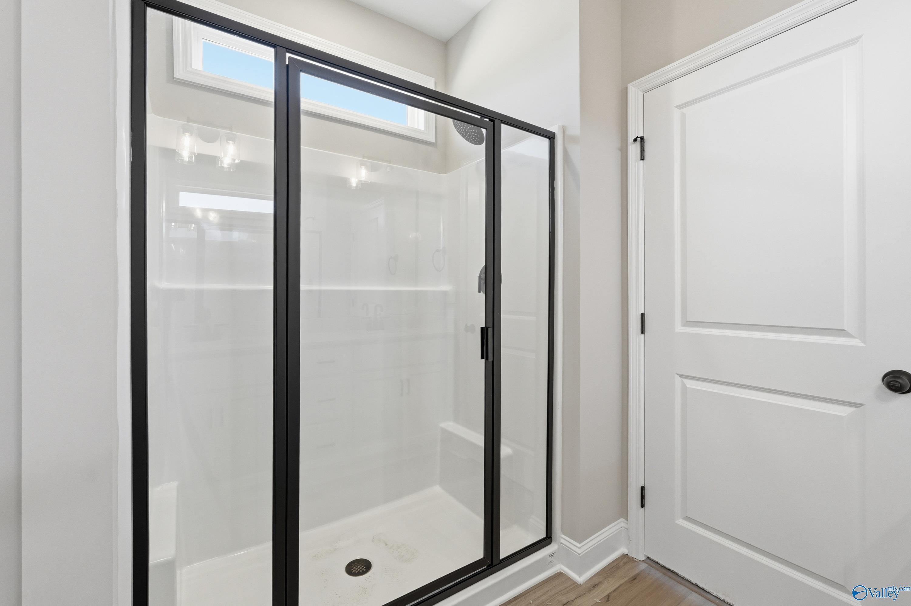 Modern glass walk-in shower with white tile, bench seat, and window in The Laurel K master bath, Davidson Homes, Cullman, AL