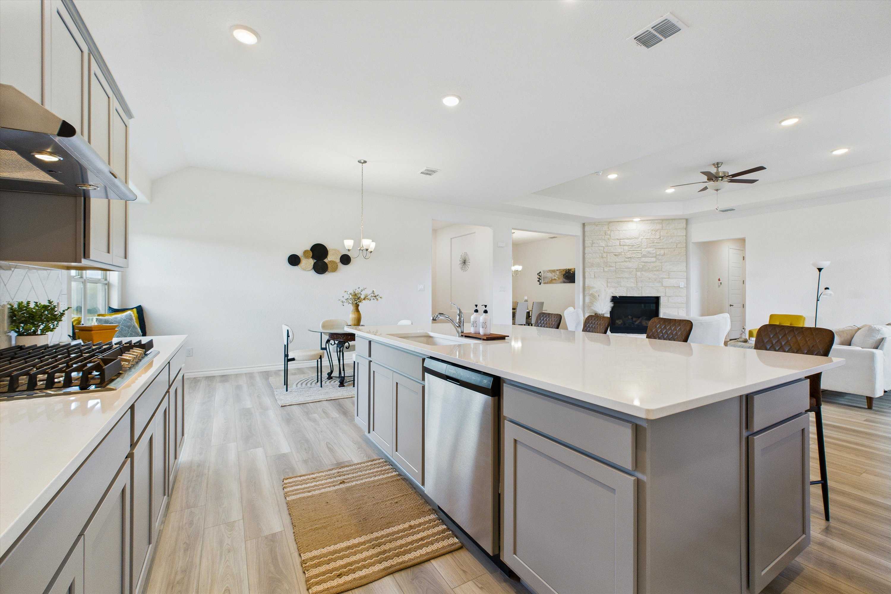 Open-concept kitchen with white island, stainless appliances, and adjacent dining-living area in Davidson Homes Summerlin C, Castroville, Texas
