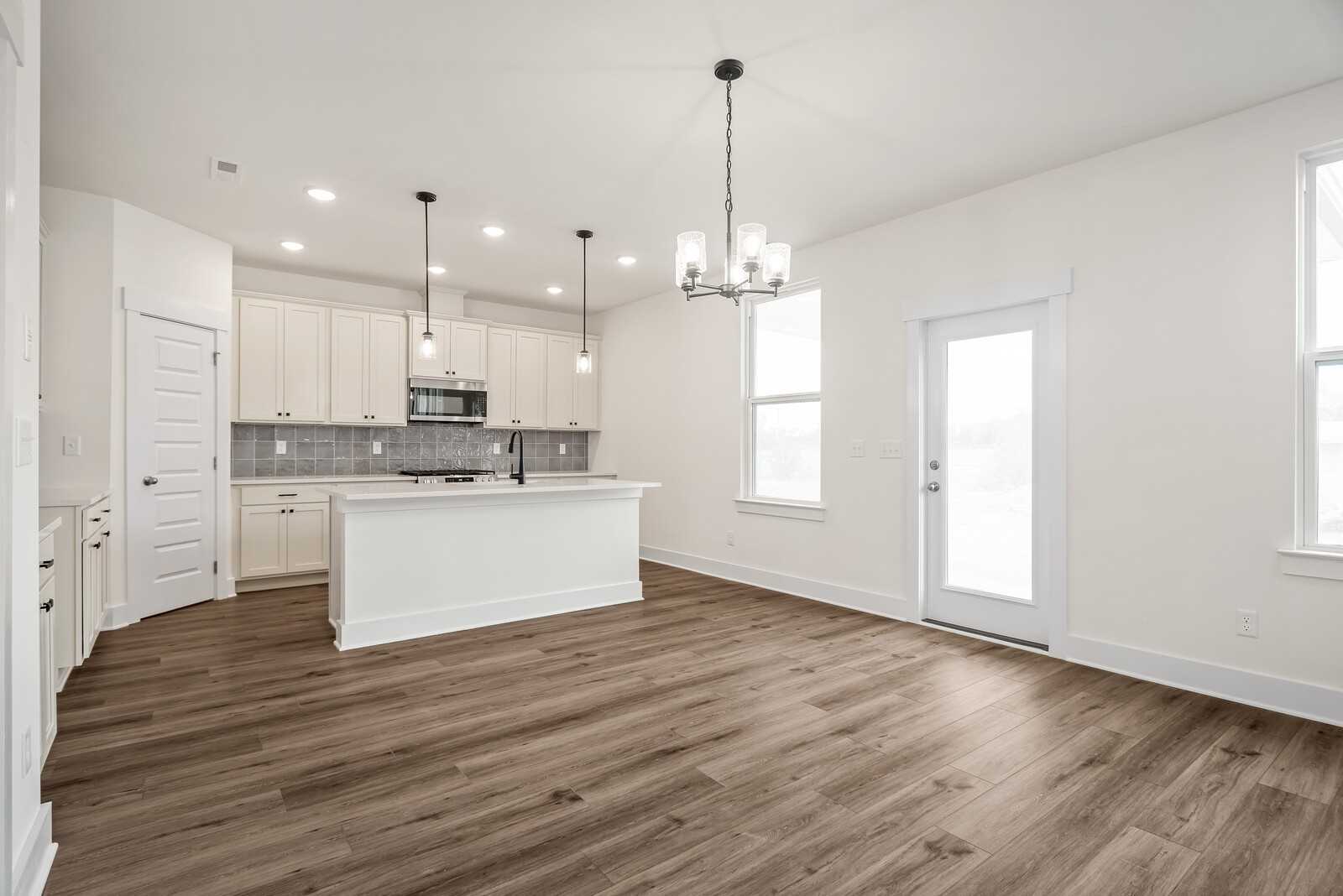 Modern open-concept kitchen with white cabinets, large island, pendant lights, and hardwood floors in The Logan C, Gallatin, TN