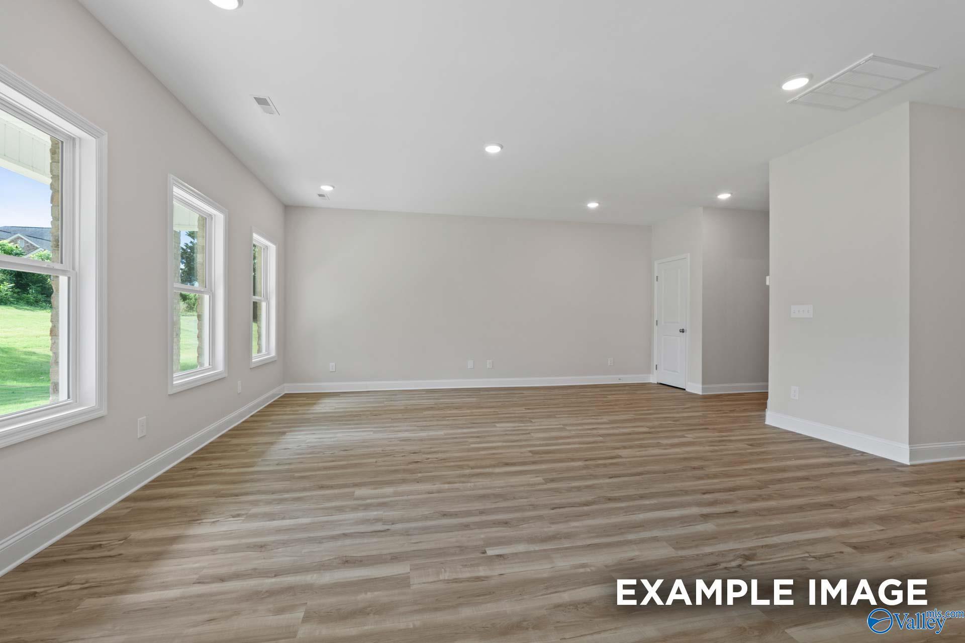 Spacious, light-filled living area with wood-style flooring in The Aiken floor plan at Jaguar Hills, Huntsville, Alabama.
