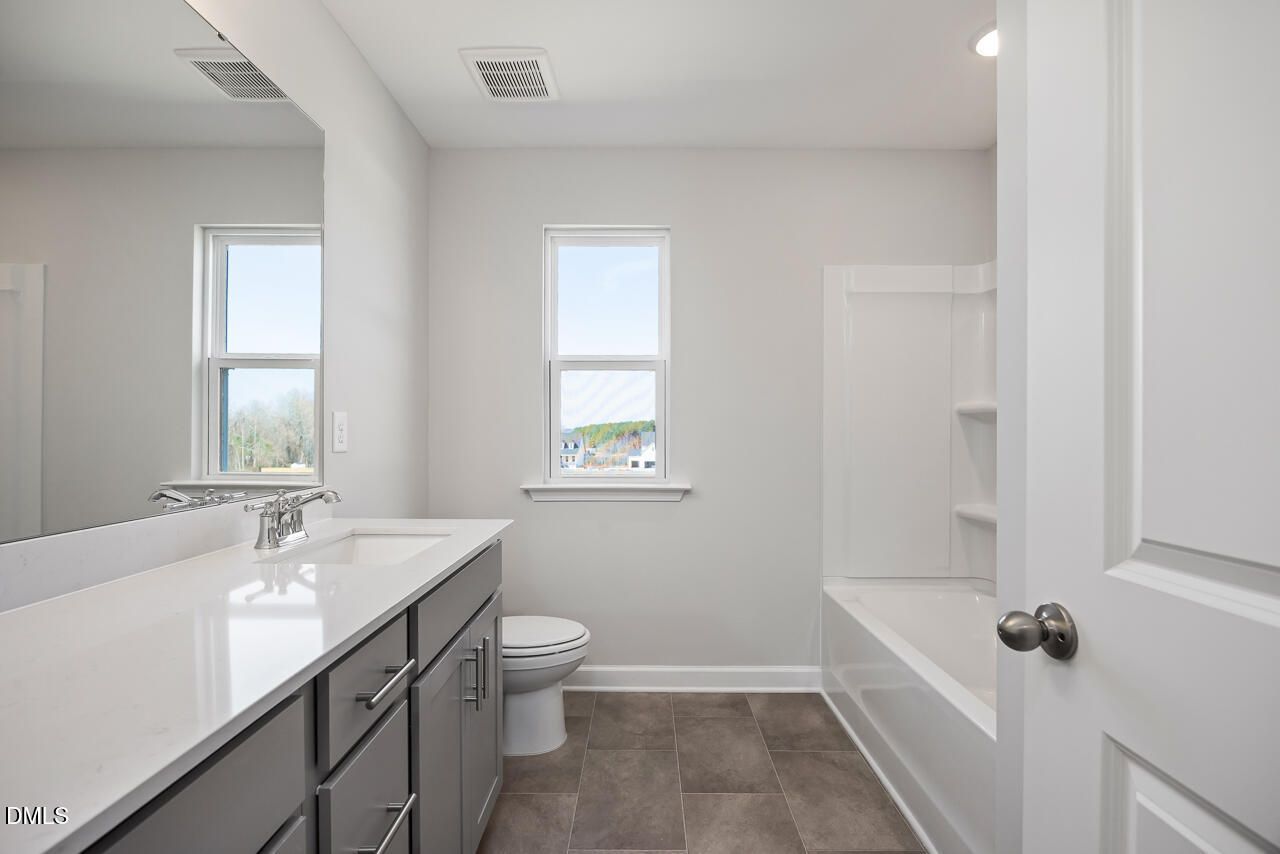 Modern bathroom with white quartz vanity, gray cabinets, soaking tub and windows in Davidson Homes The Willow G, Angier NC