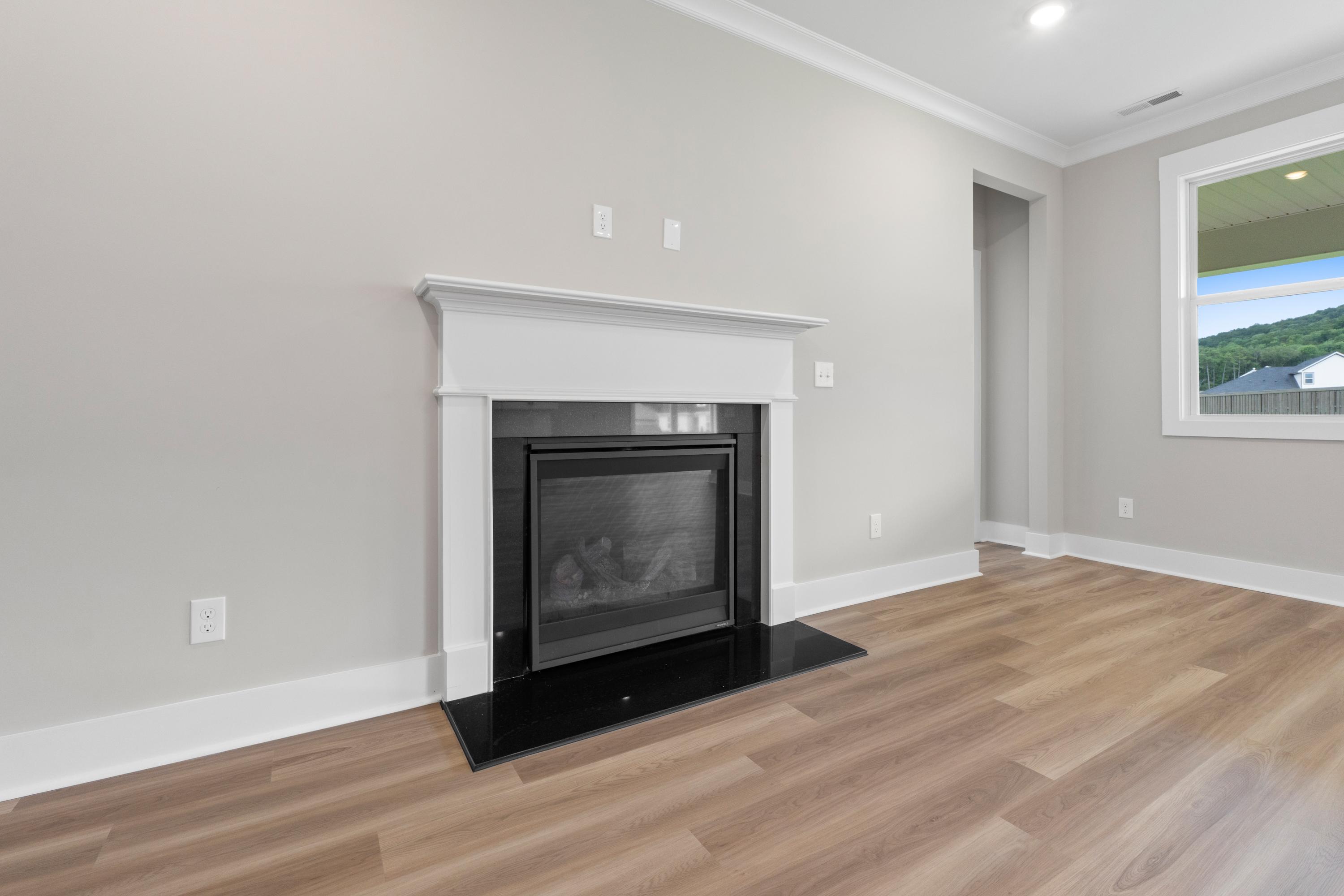 Cozy modern fireplace with white mantel in The Oxford B living room, hardwood floors, and scenic window view