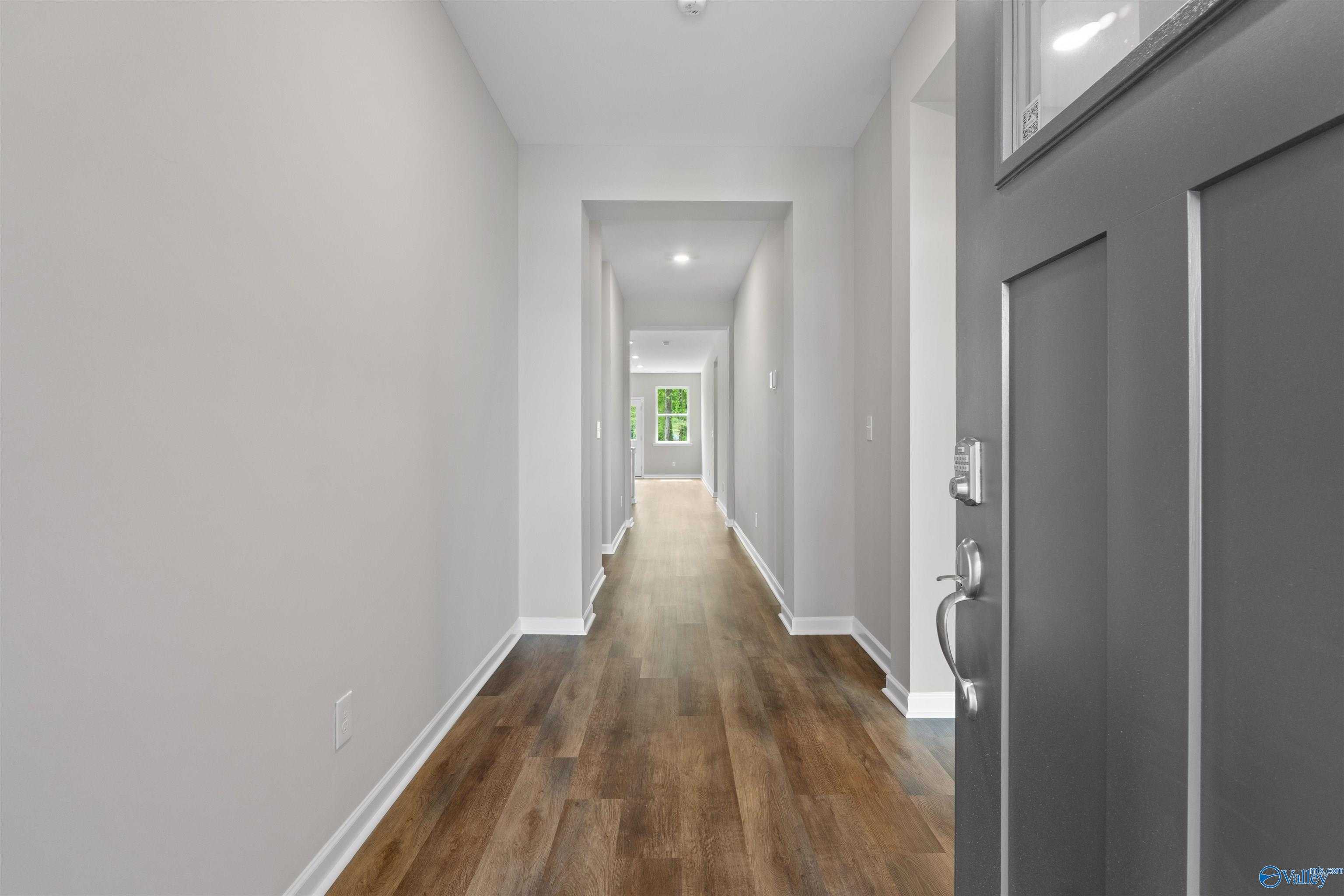 Long hallway with light gray walls, hardwood-look floors, recessed lighting, and glass-paneled entry door in Davidson Homes The Luna, Hazel Green