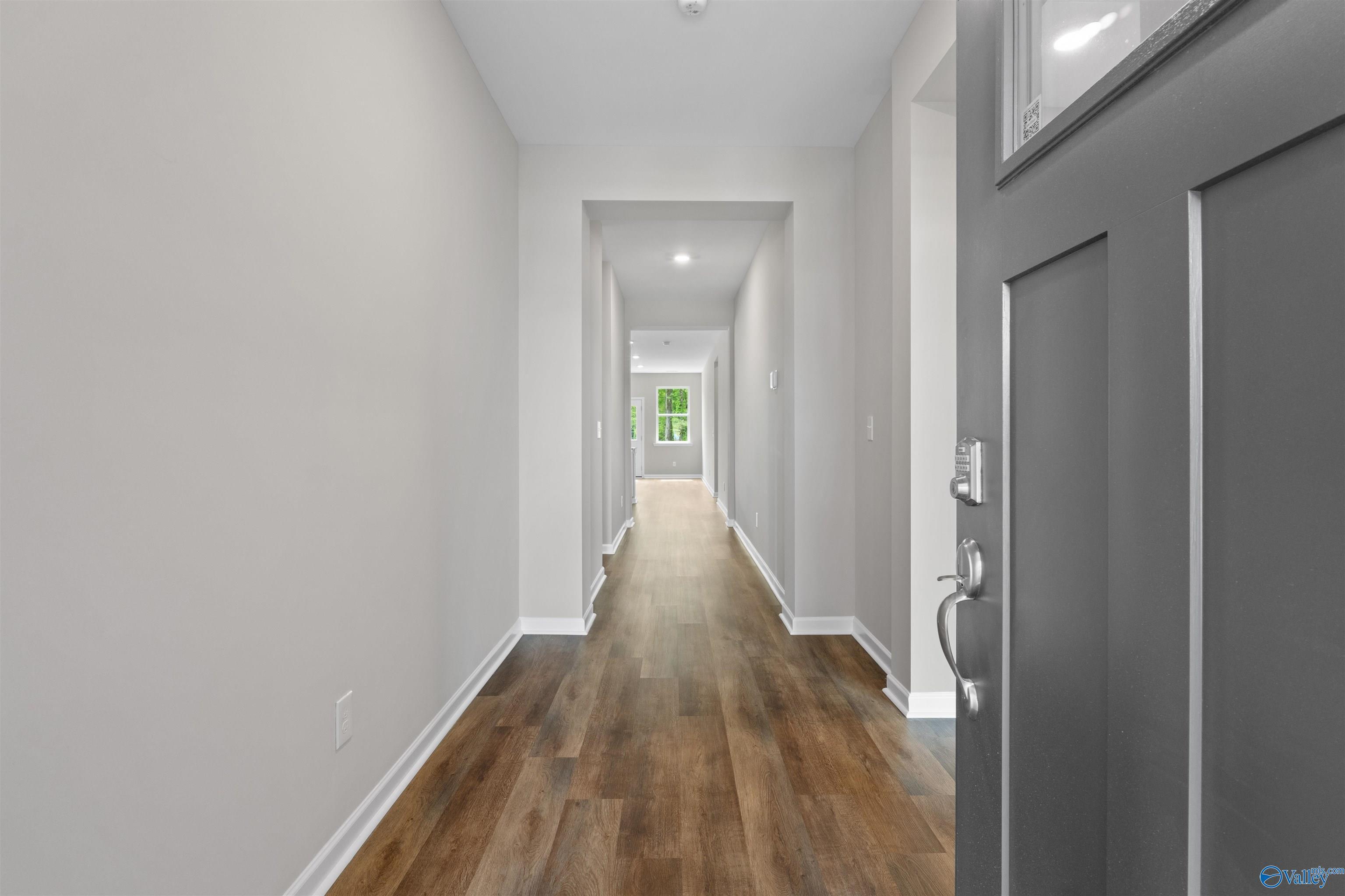 Long hallway with light gray walls, hardwood-look floors, recessed lighting, and glass-paneled entry door in Davidson Homes The Luna, Hazel Green