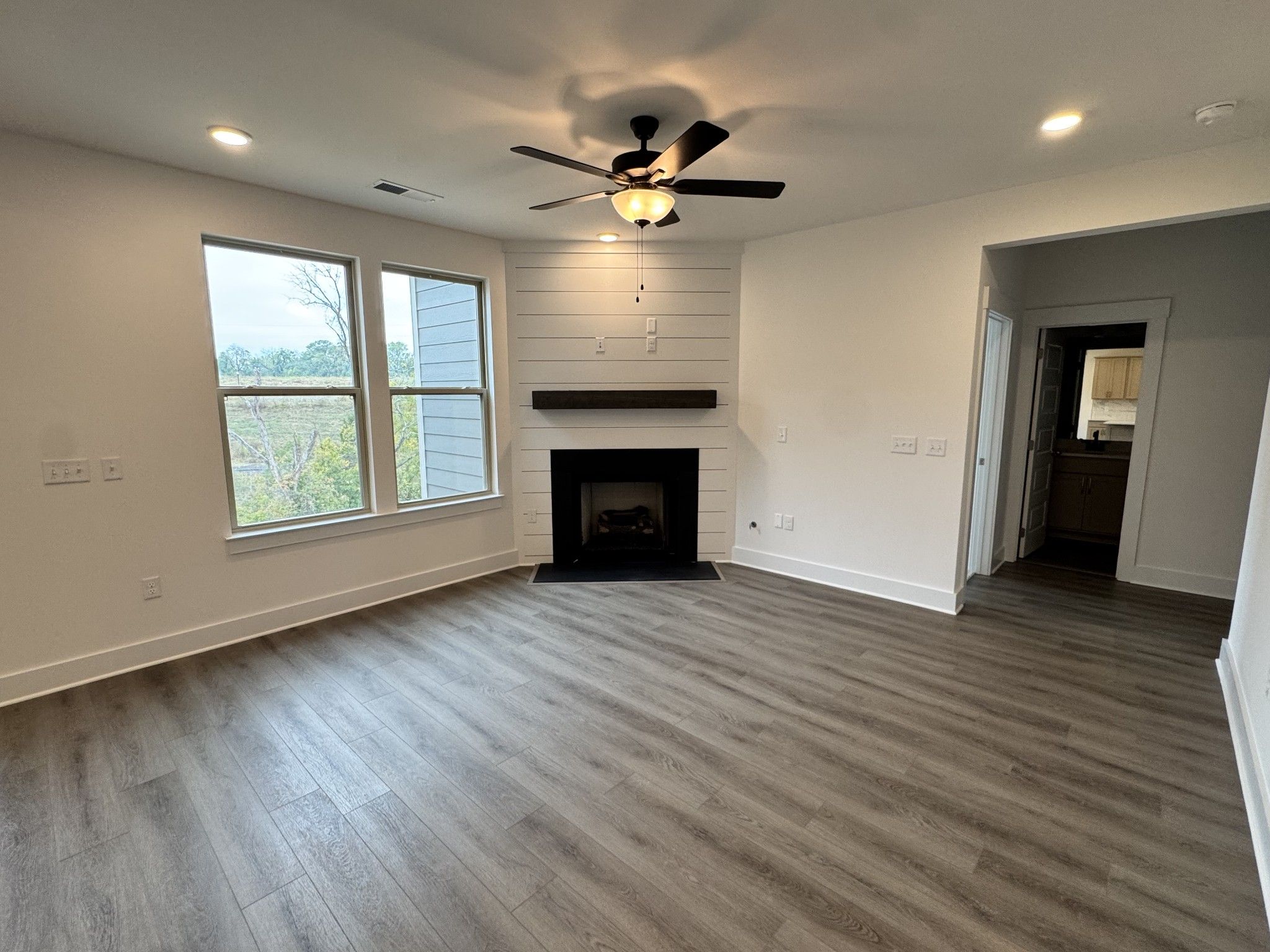 Bright living room with shiplap fireplace accent wall, ceiling fan, and luxury vinyl plank flooring in Davidson Homes Willow B, Gallatin TN