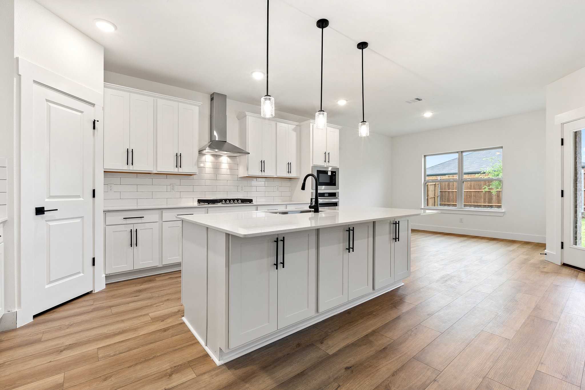 Modern white kitchen with large island, stainless appliances, subway tile backsplash in Davidson Homes Rockford C, Josephine, Texas